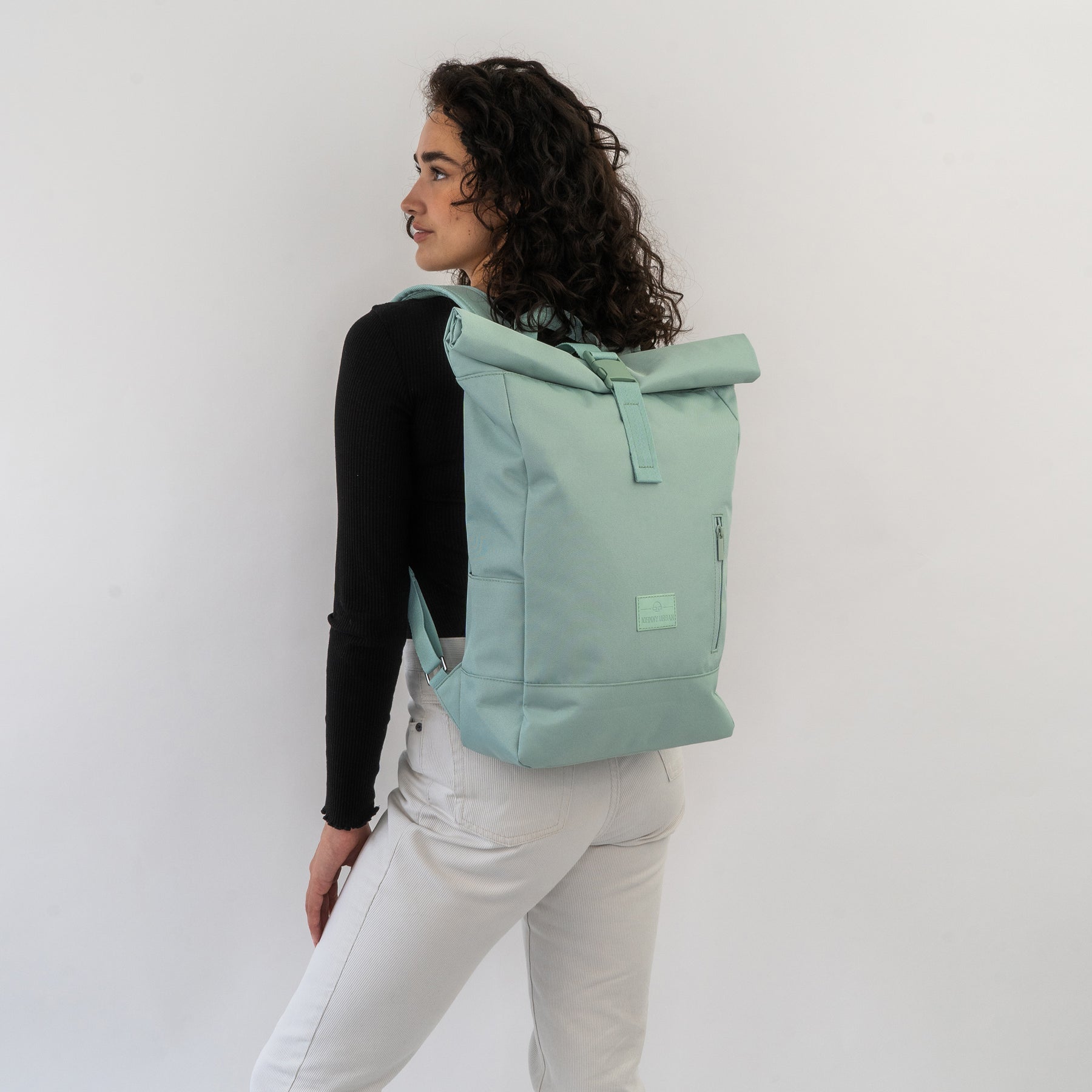 Frau mit lockigen Haaren trägt hellgrünen Rolltop-Rucksack ‚Robin Medium‘ von Johnny Urban