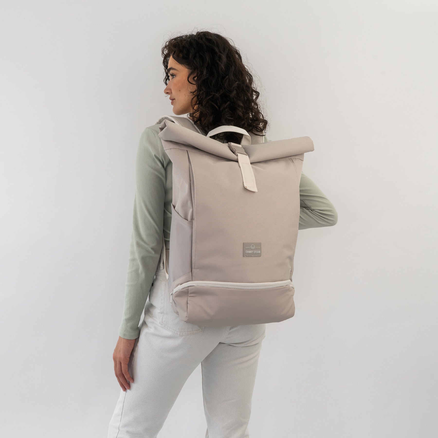Frau trägt beigen Rolltop Rucksack 'Allen Large' mit einem Verschluss und Johnny Urban Logo, seitliche Ansicht