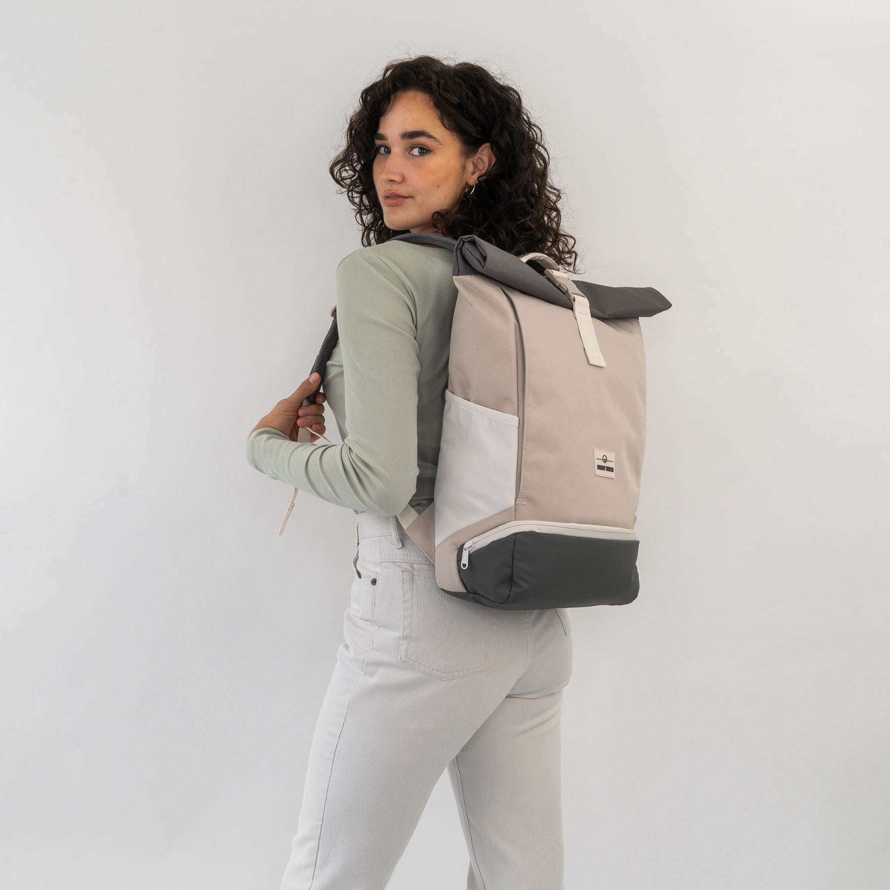 Dame mit lockigen Haaren trägt Rolltop Rucksack 'Allen Medium' in beige, weiß und grau
