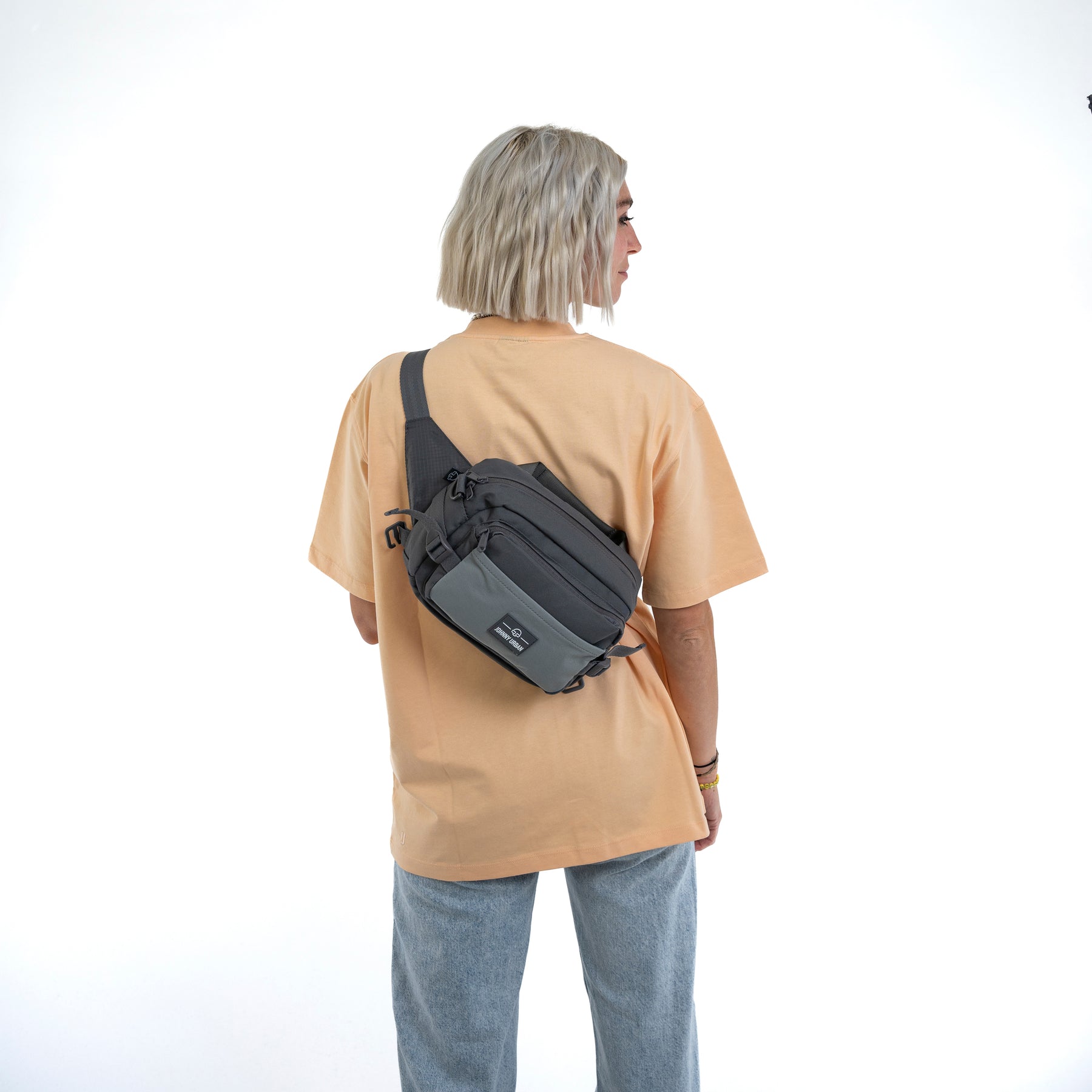 Frau mit hellblonden, kurzen gewellten Haaren trägt graue Bauchtasche 'Travis' von Johnny Urban quer über den Rücken