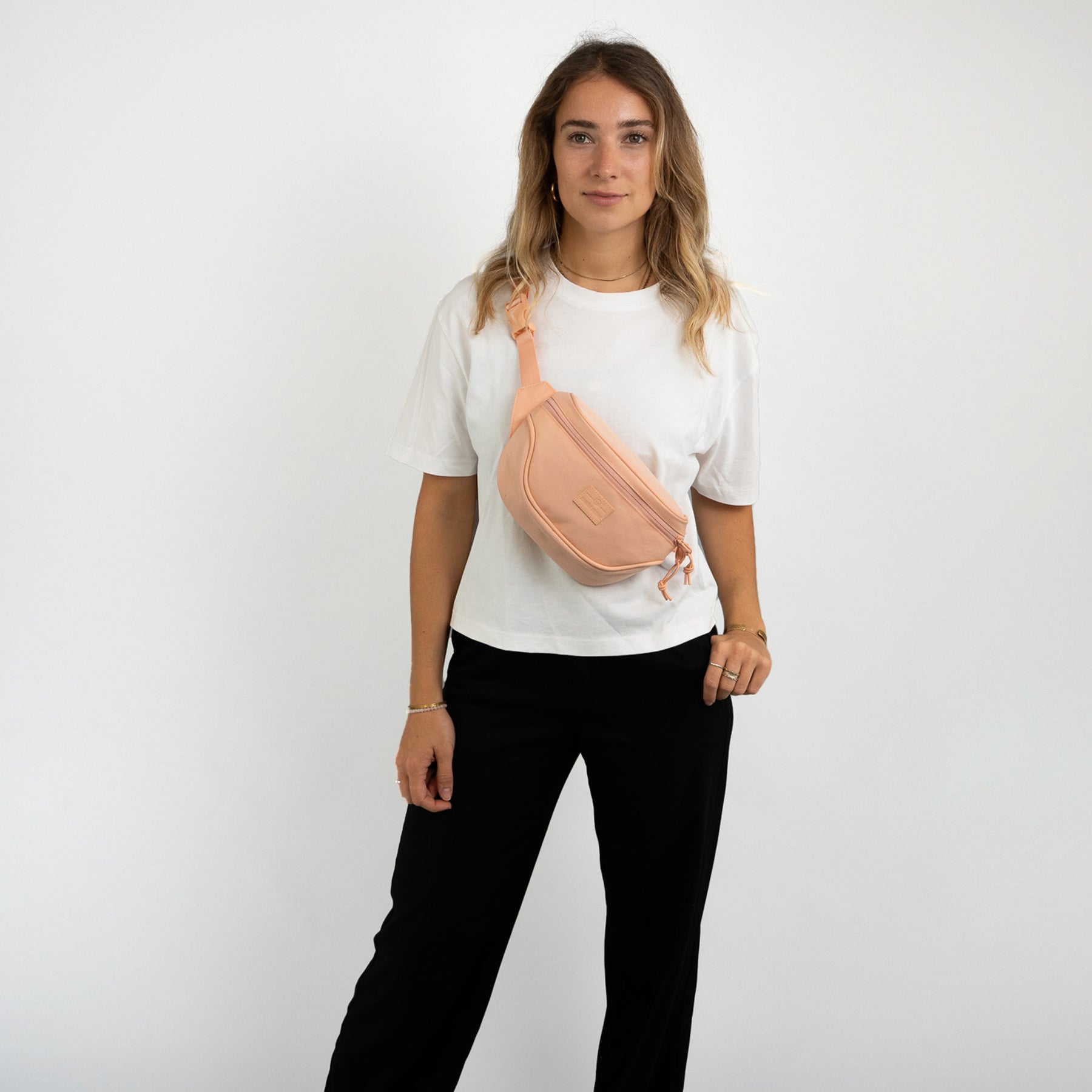 Frau trägt peachfarbene Bauchtasche 'Ben' von Johnny Urban über weiße T-Shirt und schwarze Hose