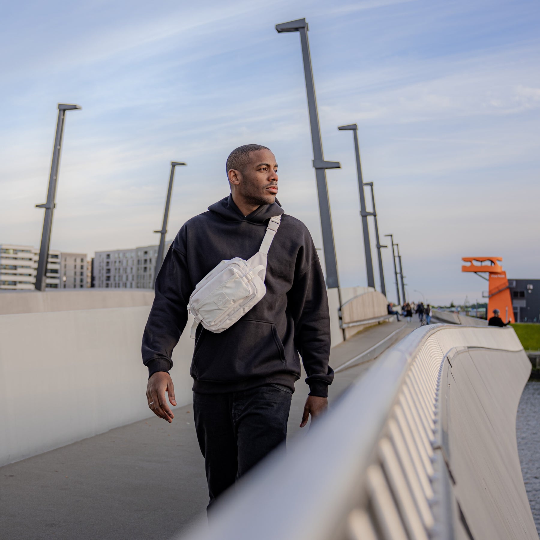 Mann trägt beigen Bauchtasche 'Travis' von Johnny Urban über schwarzem Hoodie auf urbaner Brücke
