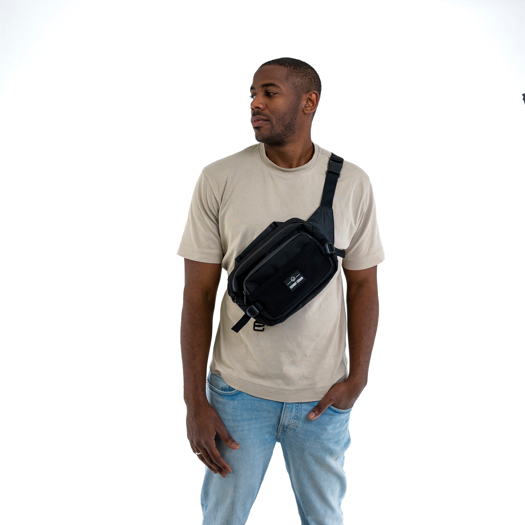 Mann trägt schwarze Johnny Urban Bauchtasche 'Travis' quer über die Brust über beigem T-Shirt und blauer Jeans