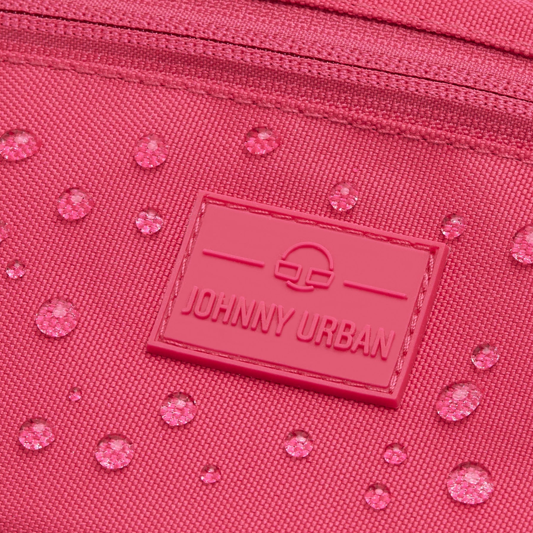 Nahaufnahme der wasserabweisenden pinkfarbenen Bauchtasche 'Ben' von Johnny Urban mit Logo-Patch und Wassertropfen