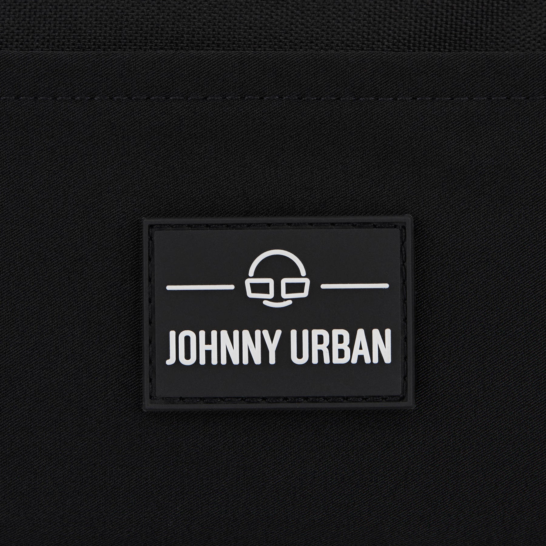 Schwarzes Logoetikett mit weißem Johnny Urban Schriftzug und minimalistischer Brillen-Motiv auf Stoff