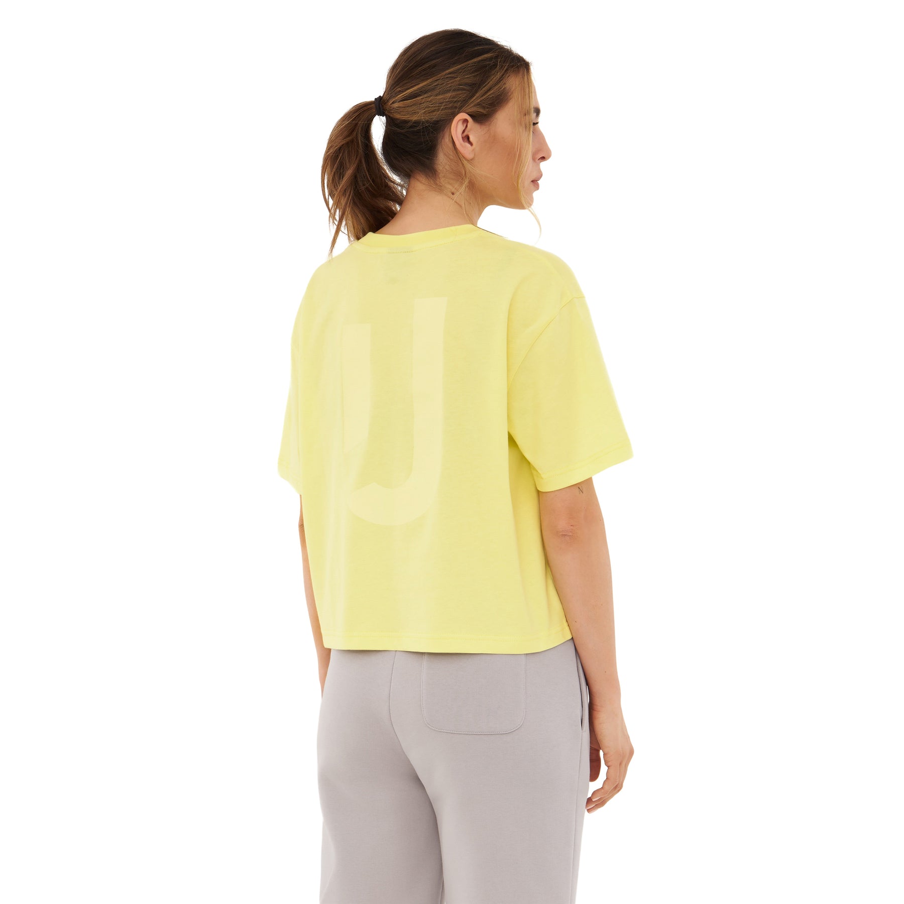 Frau trägt gelbes Cropped T-Shirt 'Zoey JU' und graue Hose, Rückansicht