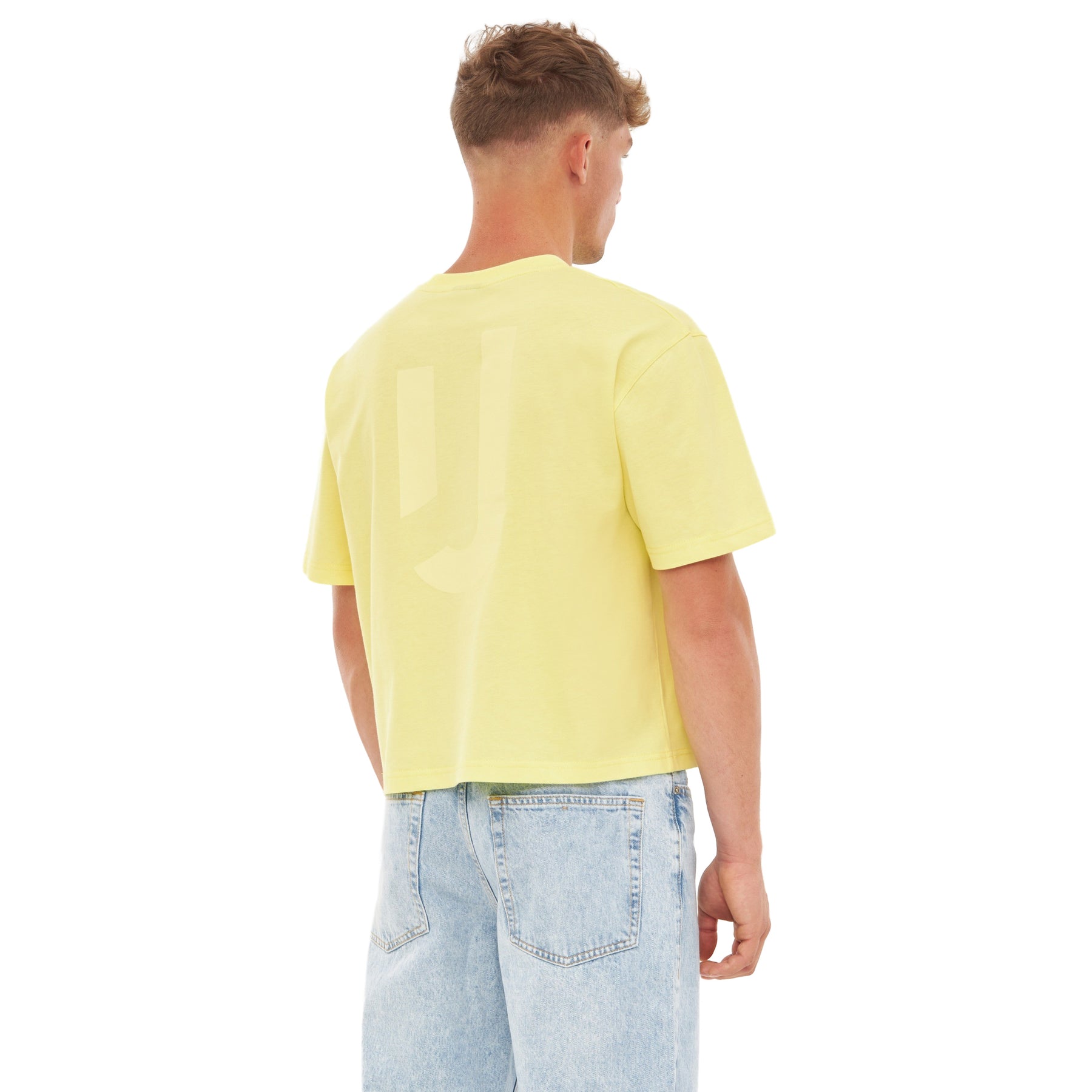 Männliches Modell trägt gelbes Cropped T-Shirt 'Zoey JU' von hinten mit hellblauen Jeans
