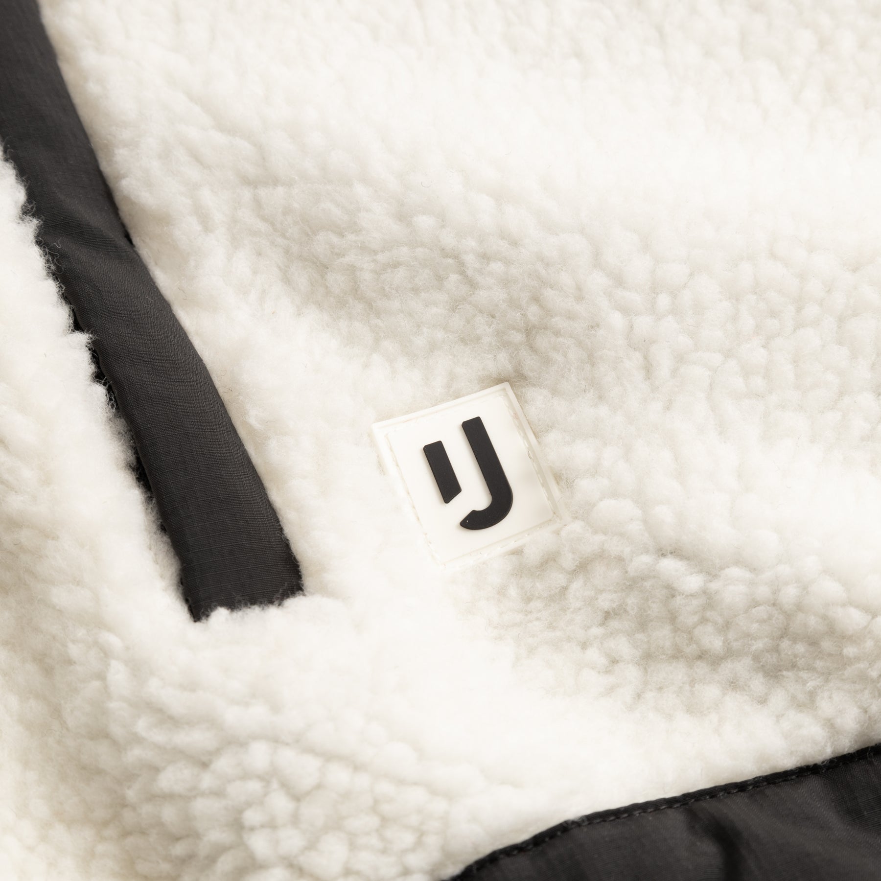 Nahaufnahme der cremefarbenen Cropped Teddy Fleecejacke 'Carey' mit Johnny Urban Logo und schwarzem Besatz