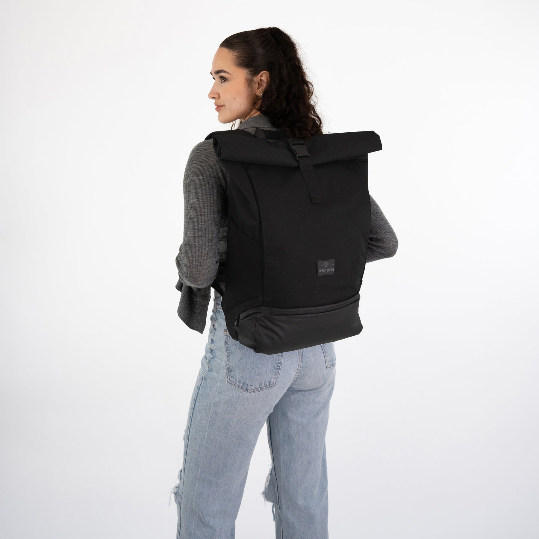 Frau mit schwarzem Rolltop Rucksack 'Allen Large' von Johnny Urban, trägt grauen Pullover und hellblaue Jeans