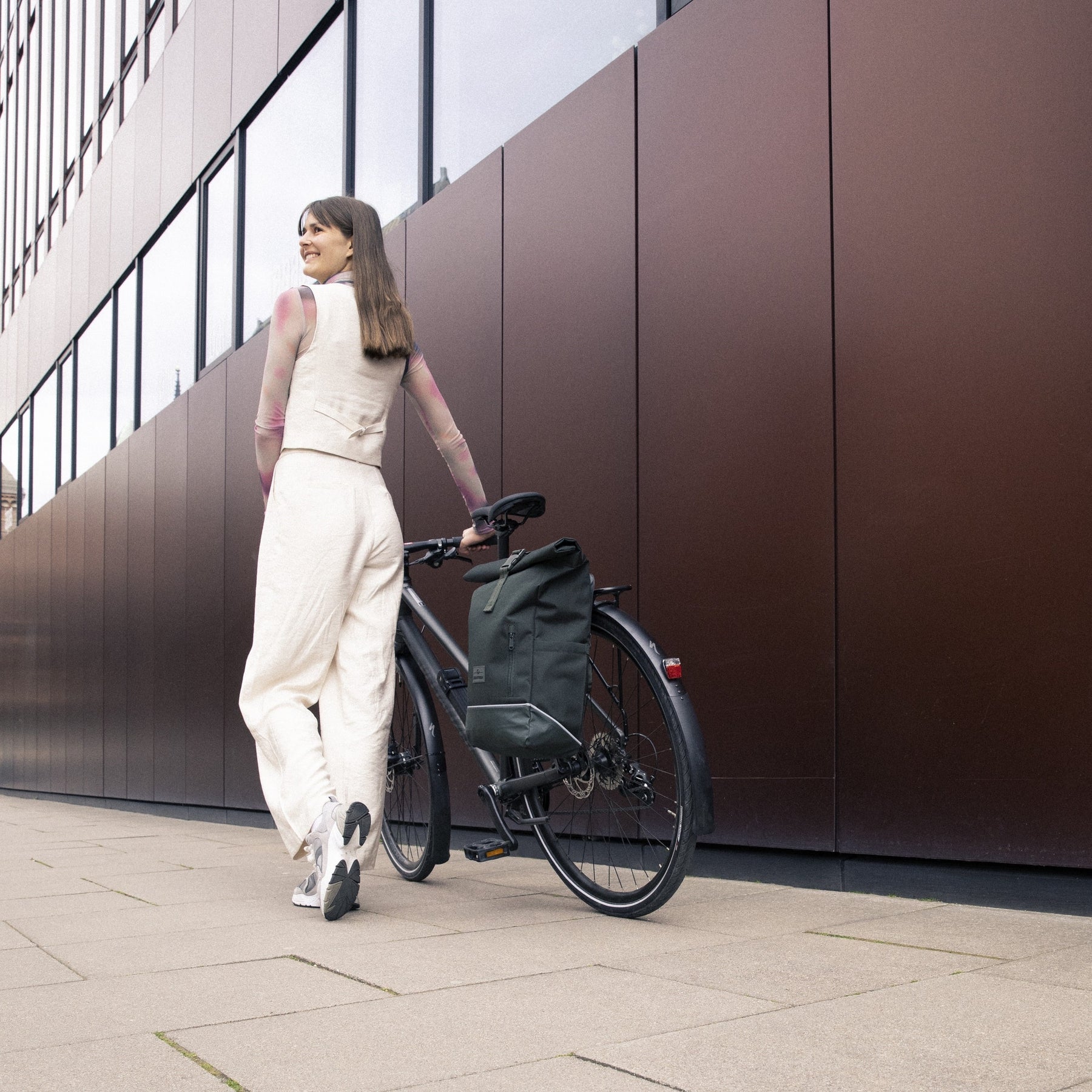 Frau schiebt Fahrrad mit dunkelgrünem Johnny Urban Rolltop Rucksack 'Robin Medium' am Gepäckträger
