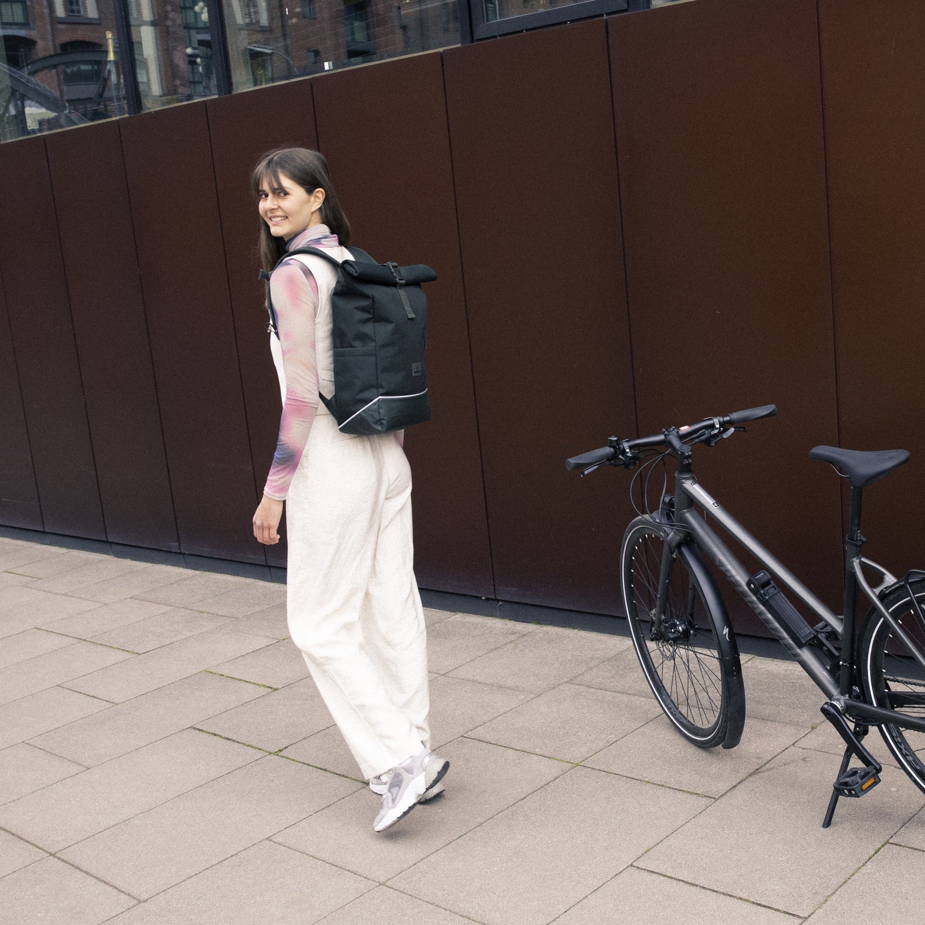 Frau trägt dunkelgrünen Rolltop Rucksack 'Robin Medium' von Johnny Urban neben Fahrrad auf urbanem Gehweg