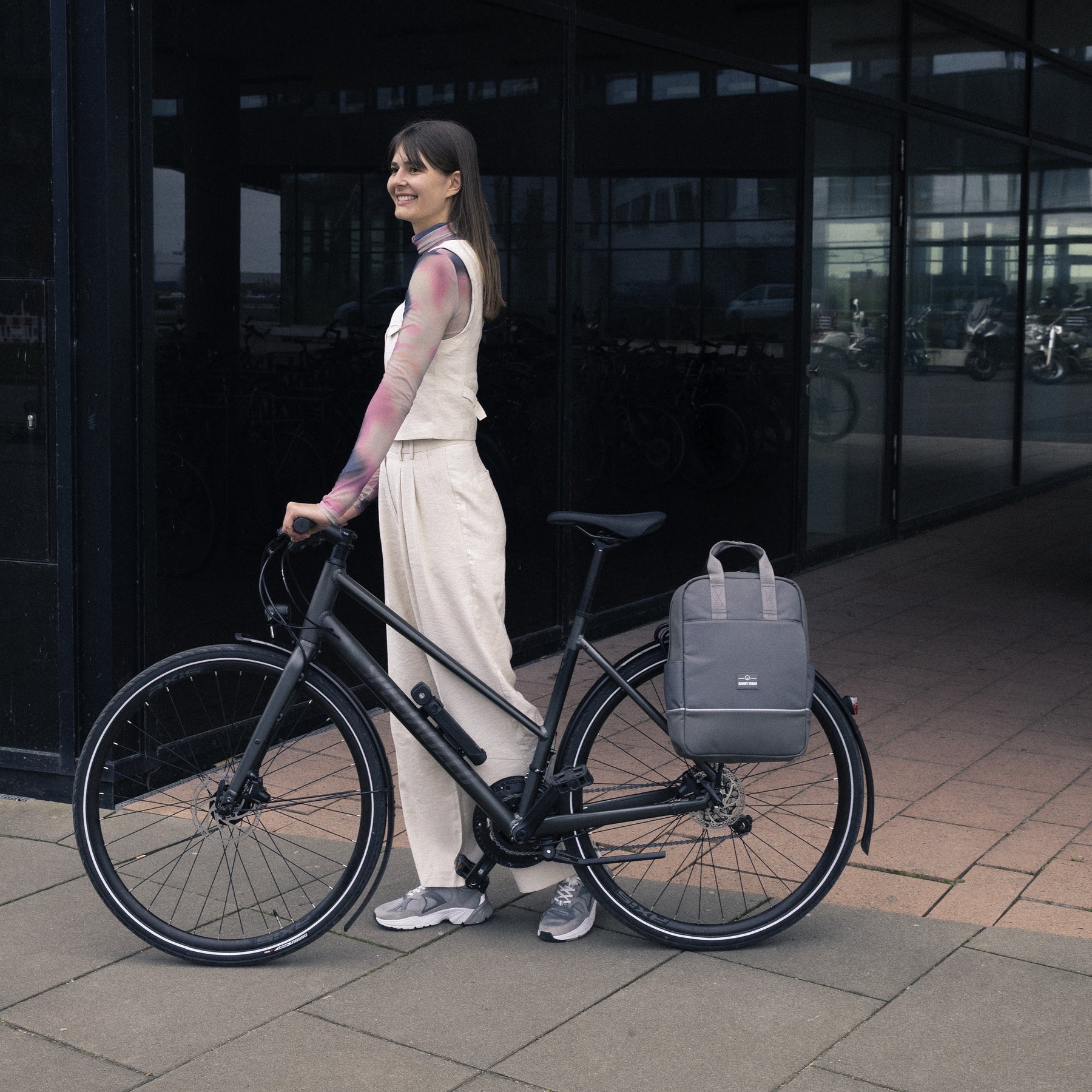 Frau steht neben Fahrrad mit grauem Rucksack 'Jona Medium' am Gepäckträger