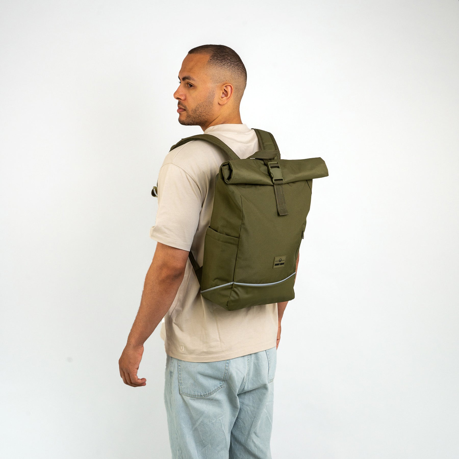 Mann trägt olivgrünen Rolltop Rucksack ‚Robin Medium‘ mit reflektierendem Streifen