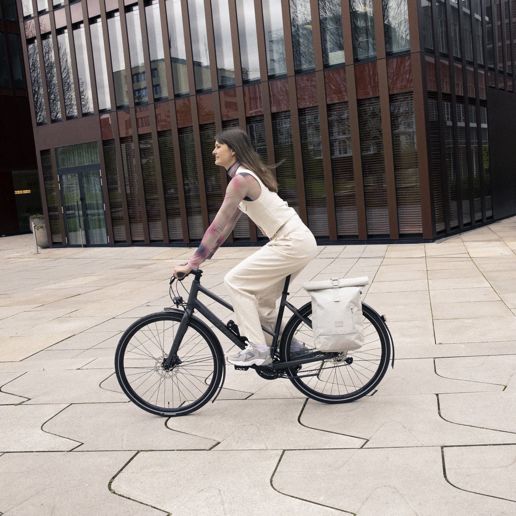 Frau fährt Fahrrad mit beigefarbenem Rolltop Rucksack 'Robin Medium' von Johnny Urban am Gepäckträger