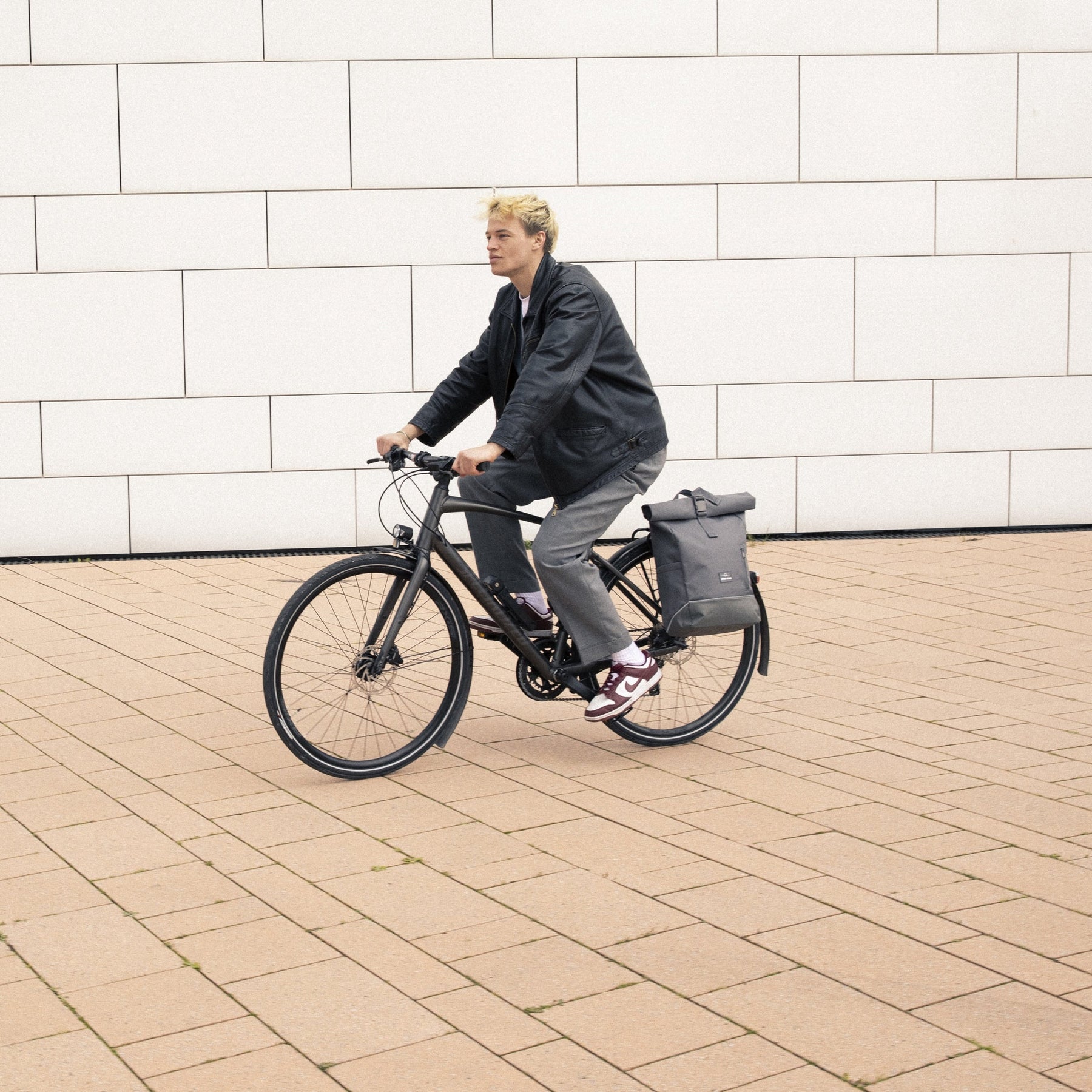 Mann fährt Fahrrad mit grauem Rolltop Rucksack 'Robin Medium' von Johnny Urban am Gepäckträger