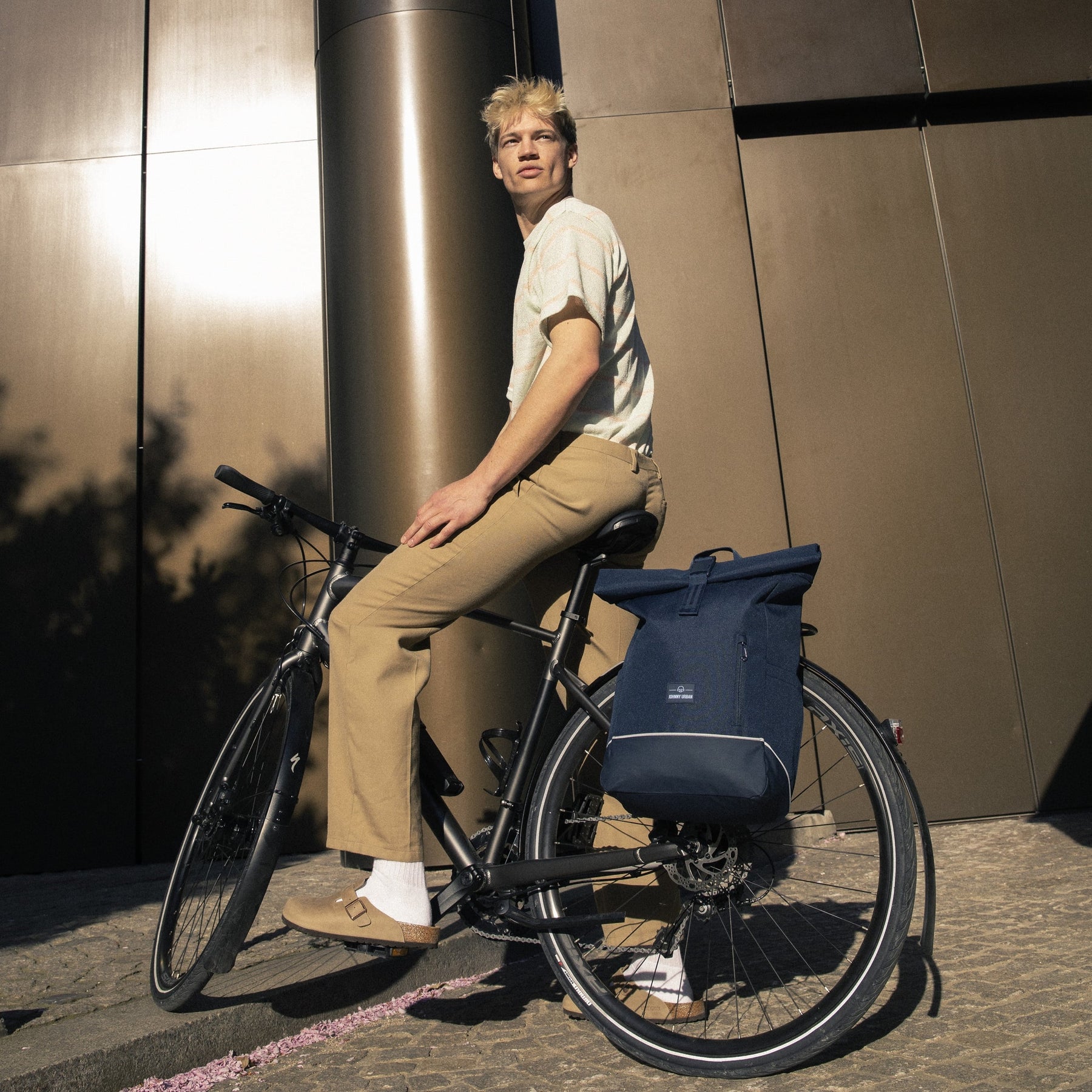 Mann sitzt auf schwarzem Fahrrad mit dunkelblauem Rolltop-Rucksack 'Robin Medium' am Gepäckträger