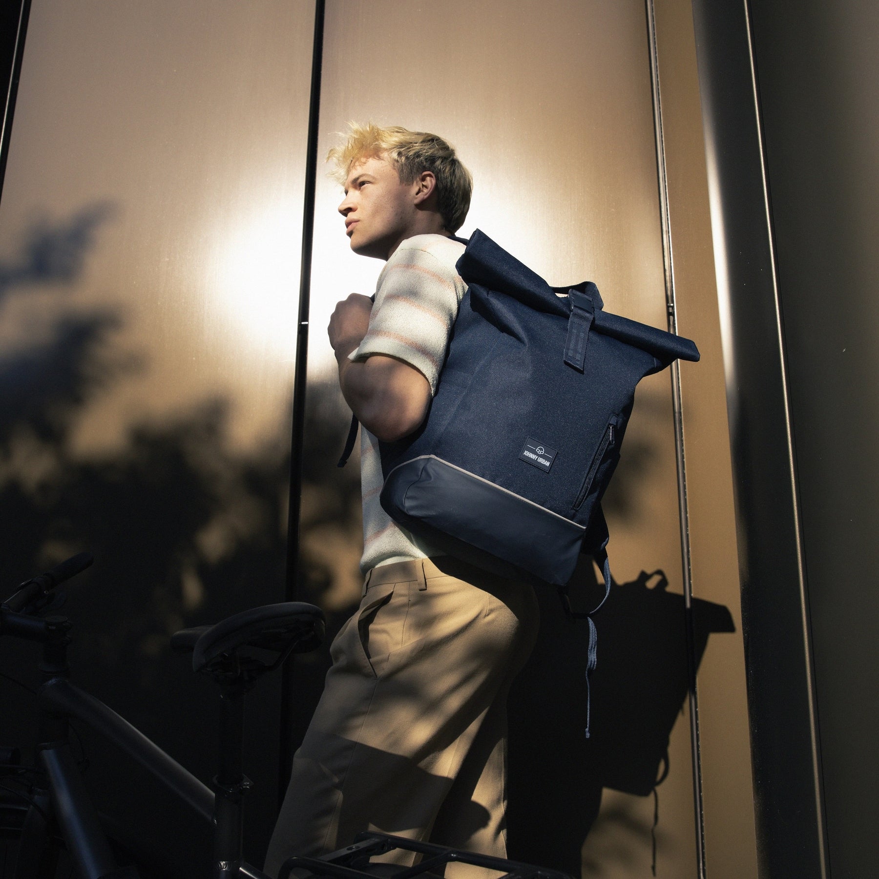 Mann trägt blauen Johnny Urban Rolltop Rucksack 'Robin Medium' neben Fahrrad