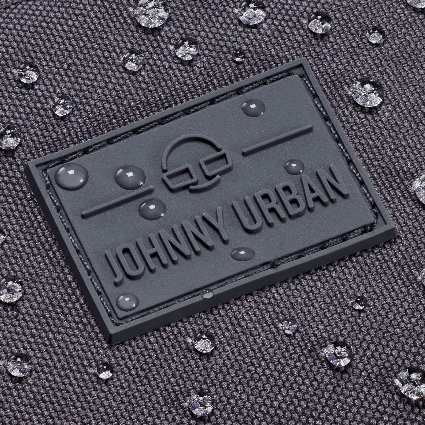 Nahe Aufnahme des wasserdichten, dunkelgrauen Materials der Bauchtasche 'Erik Large' von Johnny Urban mit Logo und Wassertropfen