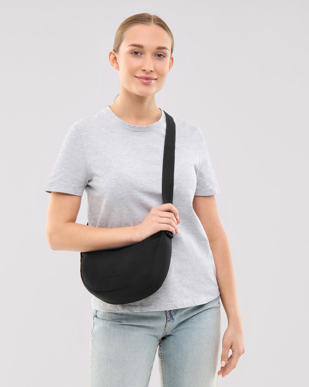 Dame trägt schwarze Half Moon Bag 'Ally Small' von Johnny Urban mit grauem T-Shirt und Jeans