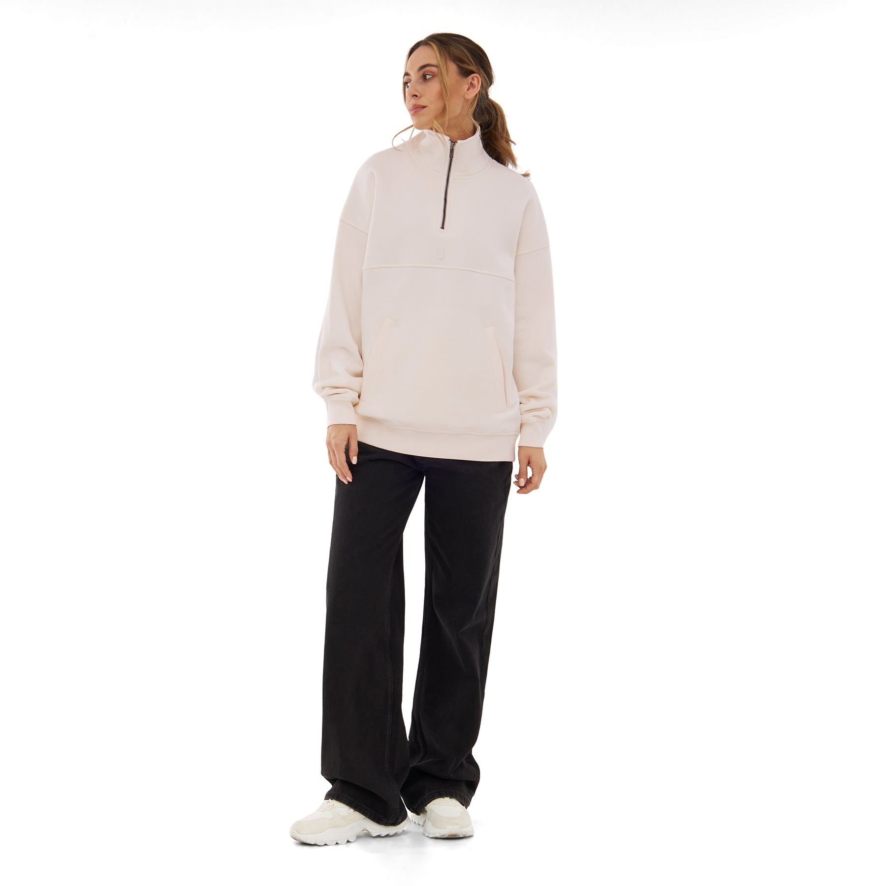 Frau trägt cremeweißen Half Zip Sweatshirt 'Cooper' mit schwarzem Reißverschluss, kombiniert mit schwarzen weiten Hosen und weißen Schuhen
