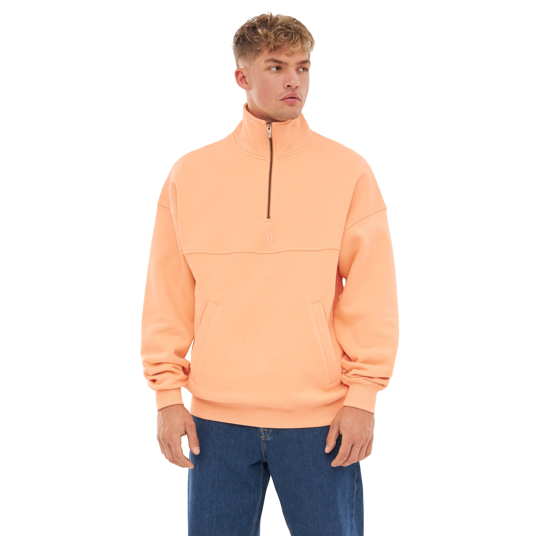Mann trägt pfirsichfarbenen Halb-Zip-Sweatshirt 'Cooper' mit Stehkragen und Reißverschluss, kombiniert mit blauer Jeans
