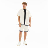 Mann trägt cremefarbenes Set 'Parker' mit kurzärmeligem Hemd und Shorts mit dunklen Streifen, weiße Sneakers