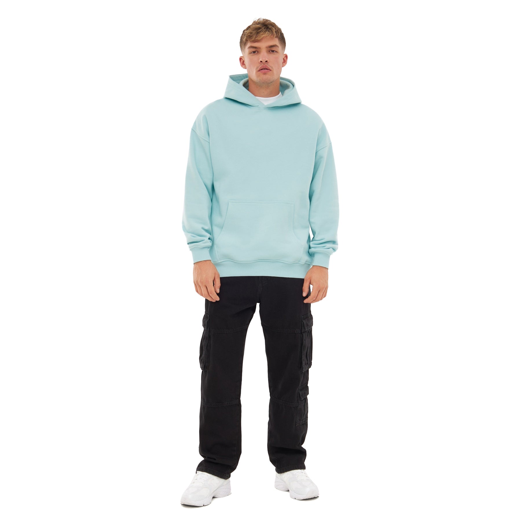 Mann trägt oversized Hoodie 'Cody' in eisblau mit schwarzer Cargo-Hose und weißen Sneakern