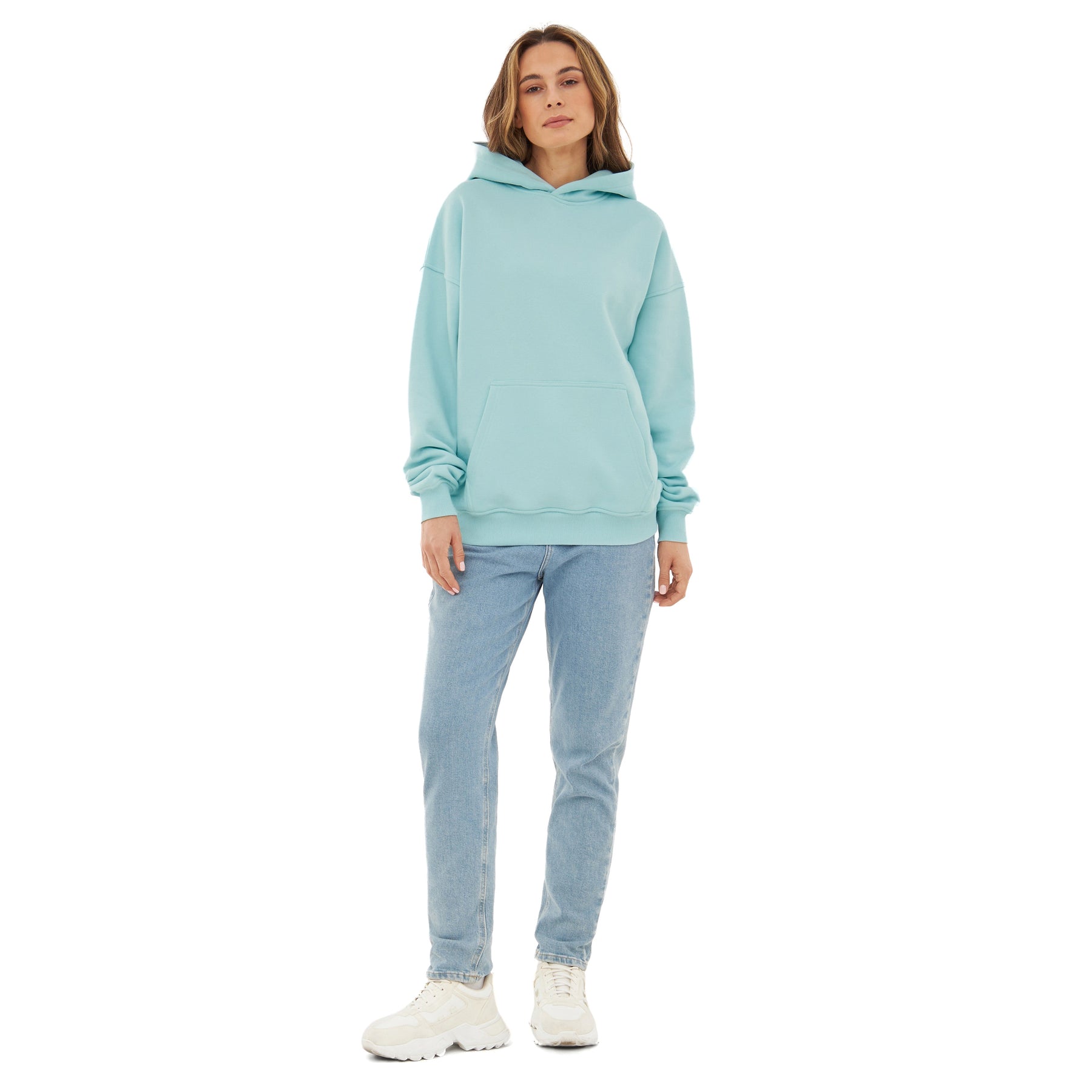 Frau trägt oversized Hoodie 'Cody' in eisblau mit großer Tasche vorne, dazu helle Jeans und weiße Sneaker