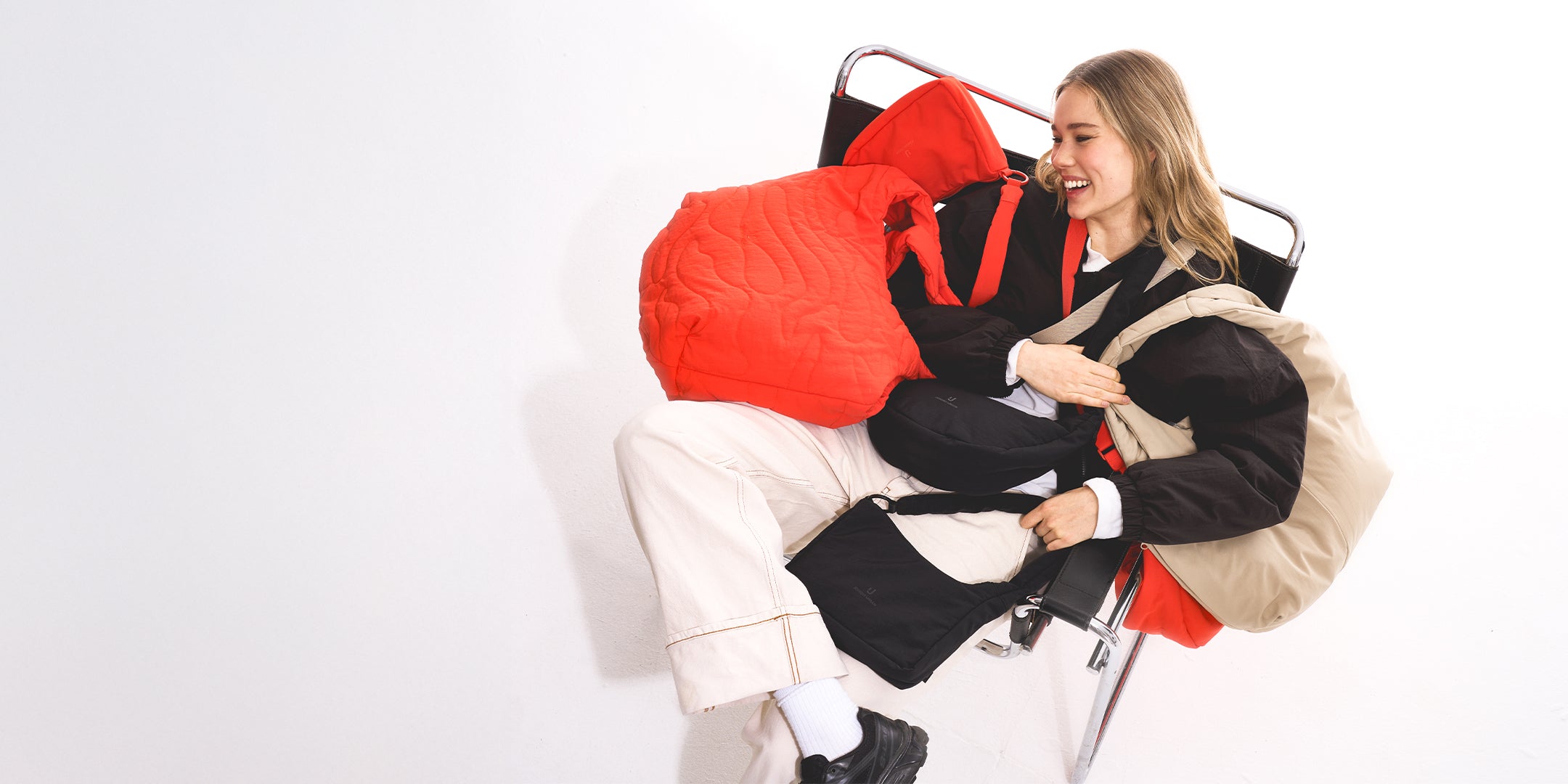 Frau sitzt mit einem Lachen im Sessel und hat alle Johnny Urban Taschen über sich gelegt.