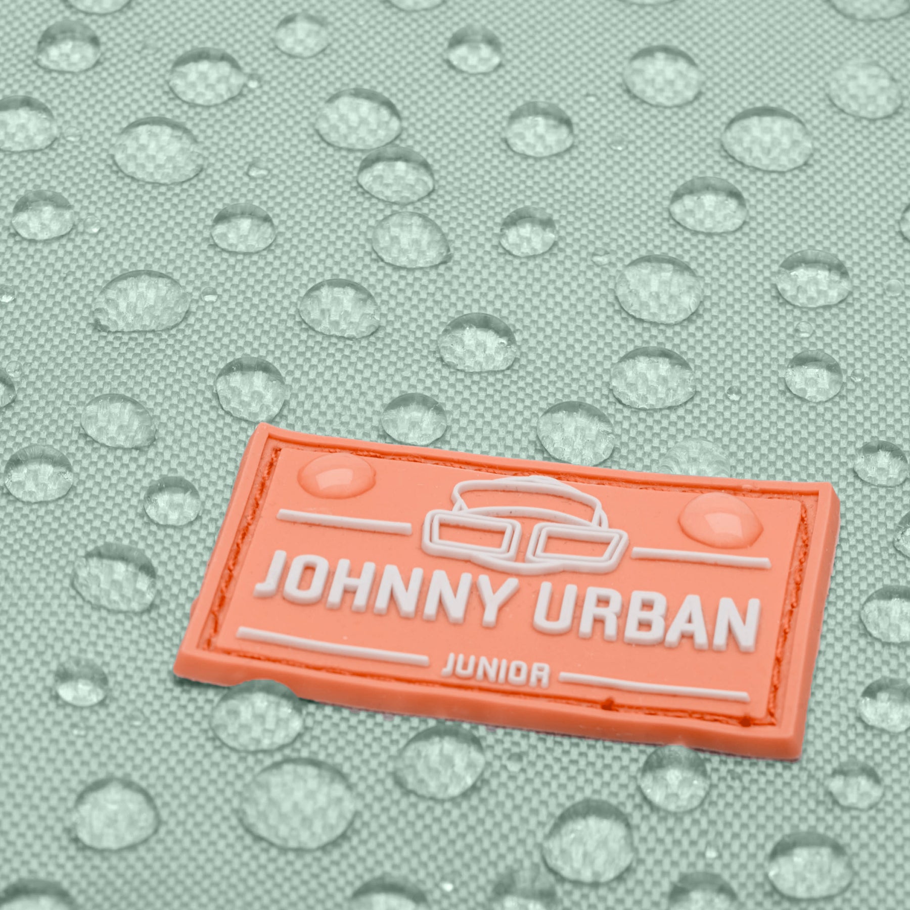 Nahaufnahme eines mintfarbenen Kinder-Turnbeutels mit orangefarbenem Johnny Urban Junior Logo und Wassertropfen