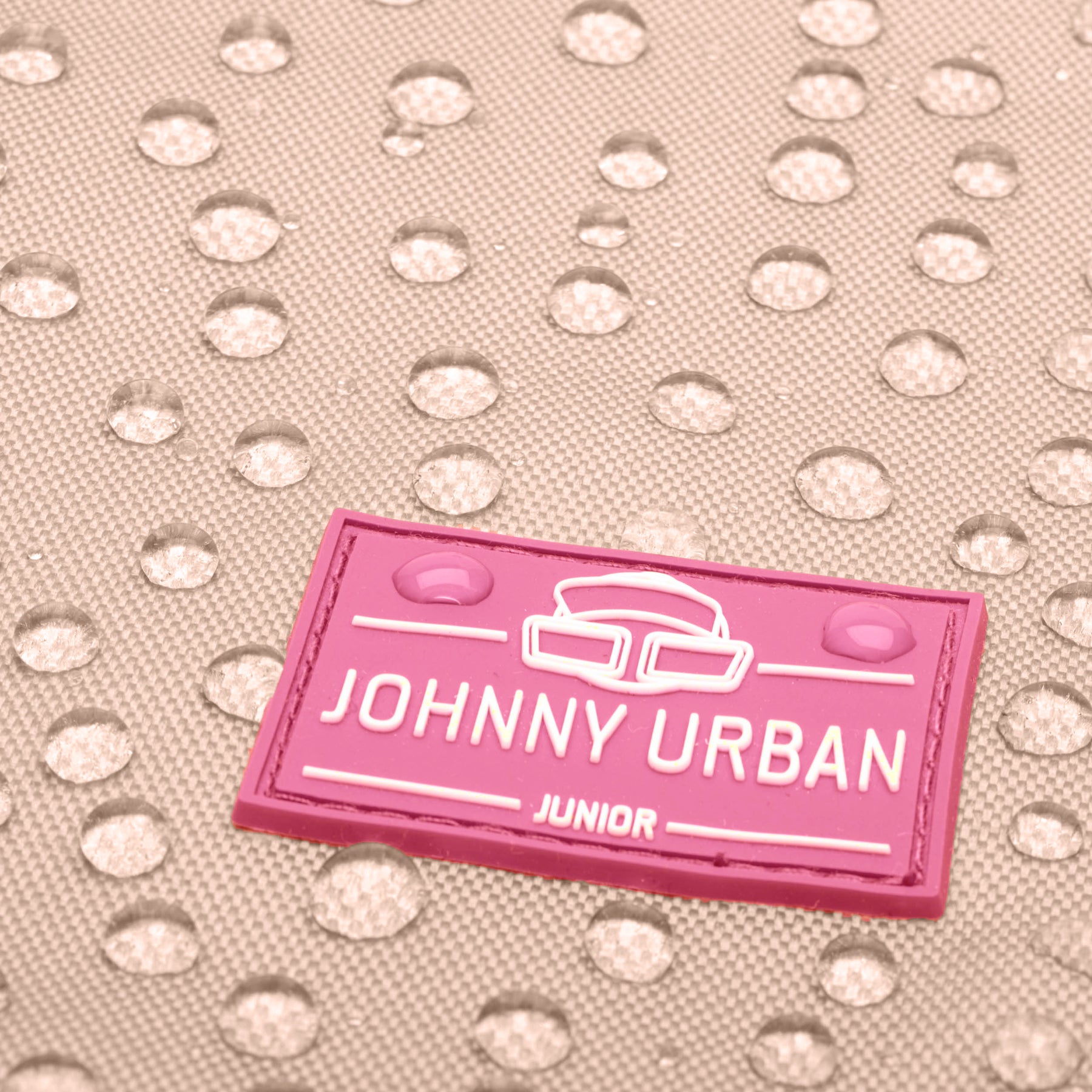 Nahaufnahme eines wasserabweisenden Materials mit zwei Wassertropfen auf einem rosa Johnny Urban Junior Etikett