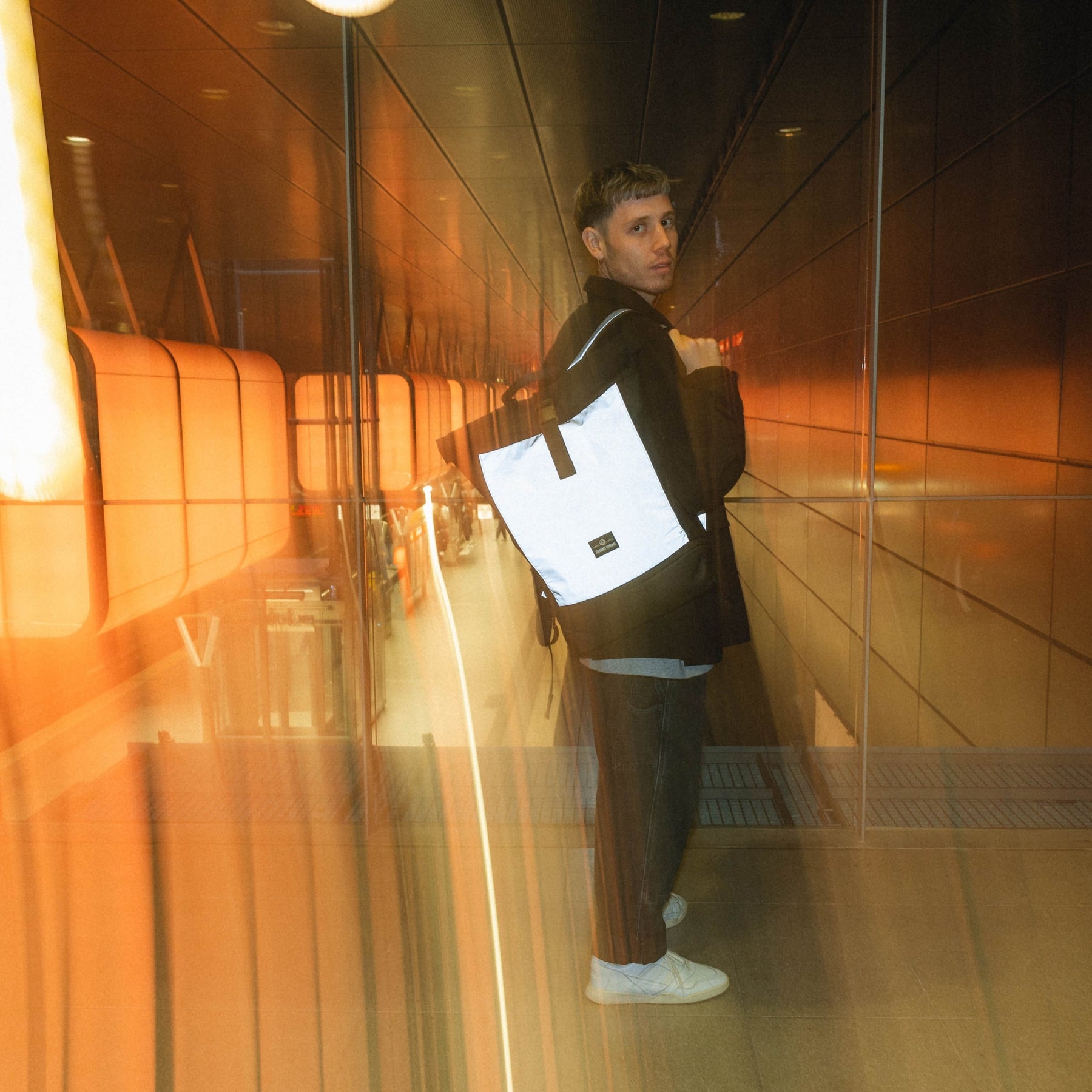 Mann trägt reflektierenden Rolltop Rucksack 'Allen Large' von Johnny Urban in urbanem, beleuchtetem Tunnel
