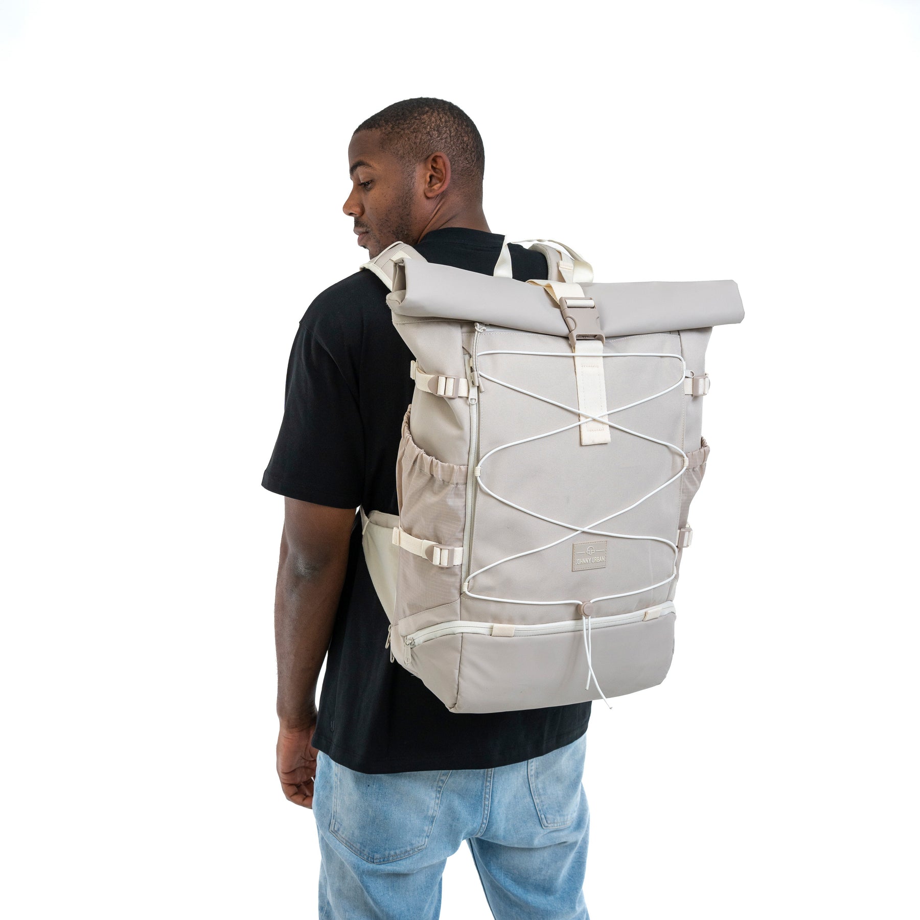 Mann mit schwarzem T-Shirt und Jeans trägt beigefarbenen Johnny Urban Reiserucksack 'Allen Large Travel' mit gerolltem Verschluss und elastischen Schnüren