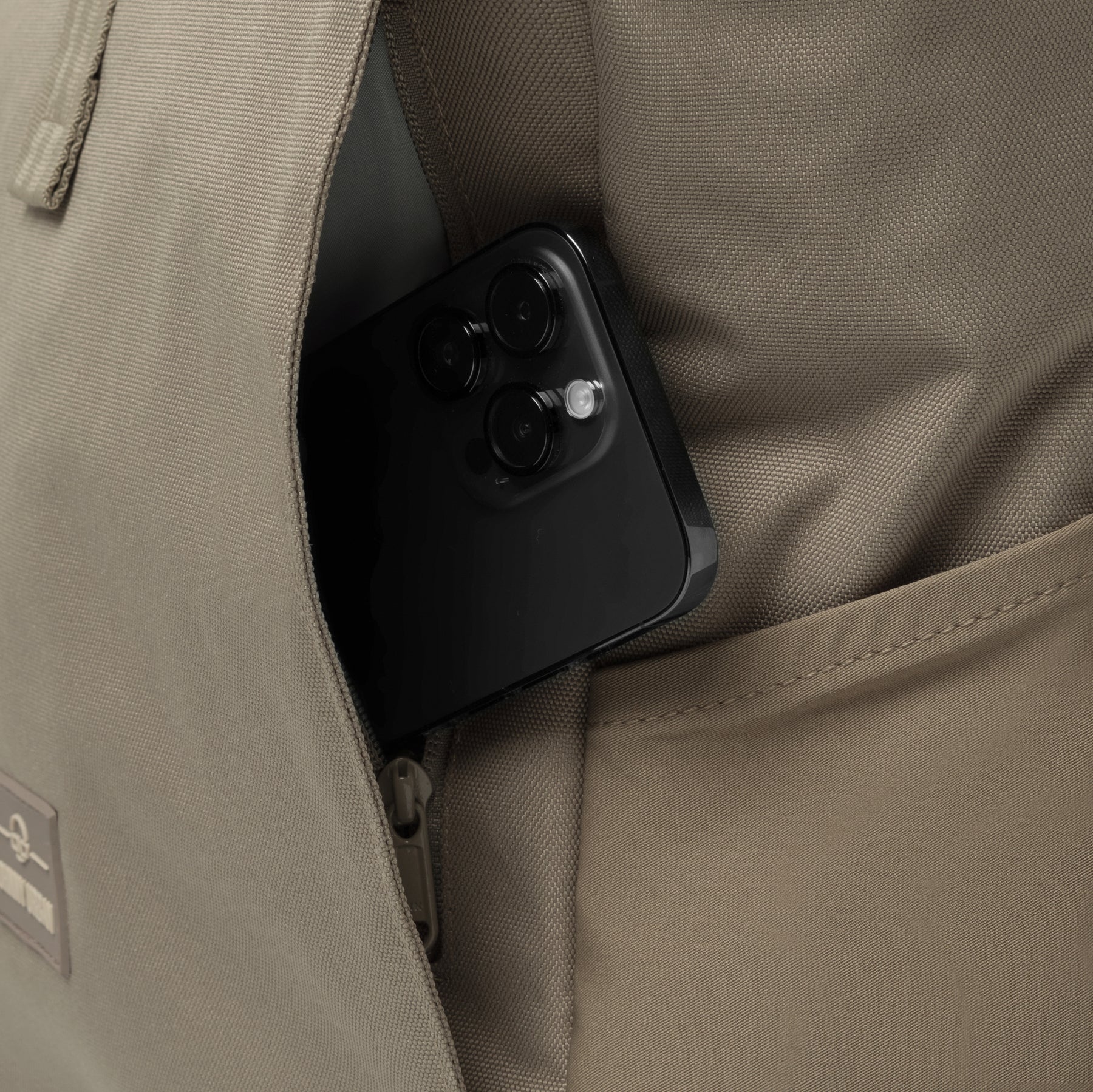 Rolltop Rucksack Allen Large in Braun mit offenem Geheimfach und steckendem schwarzen Smartphone