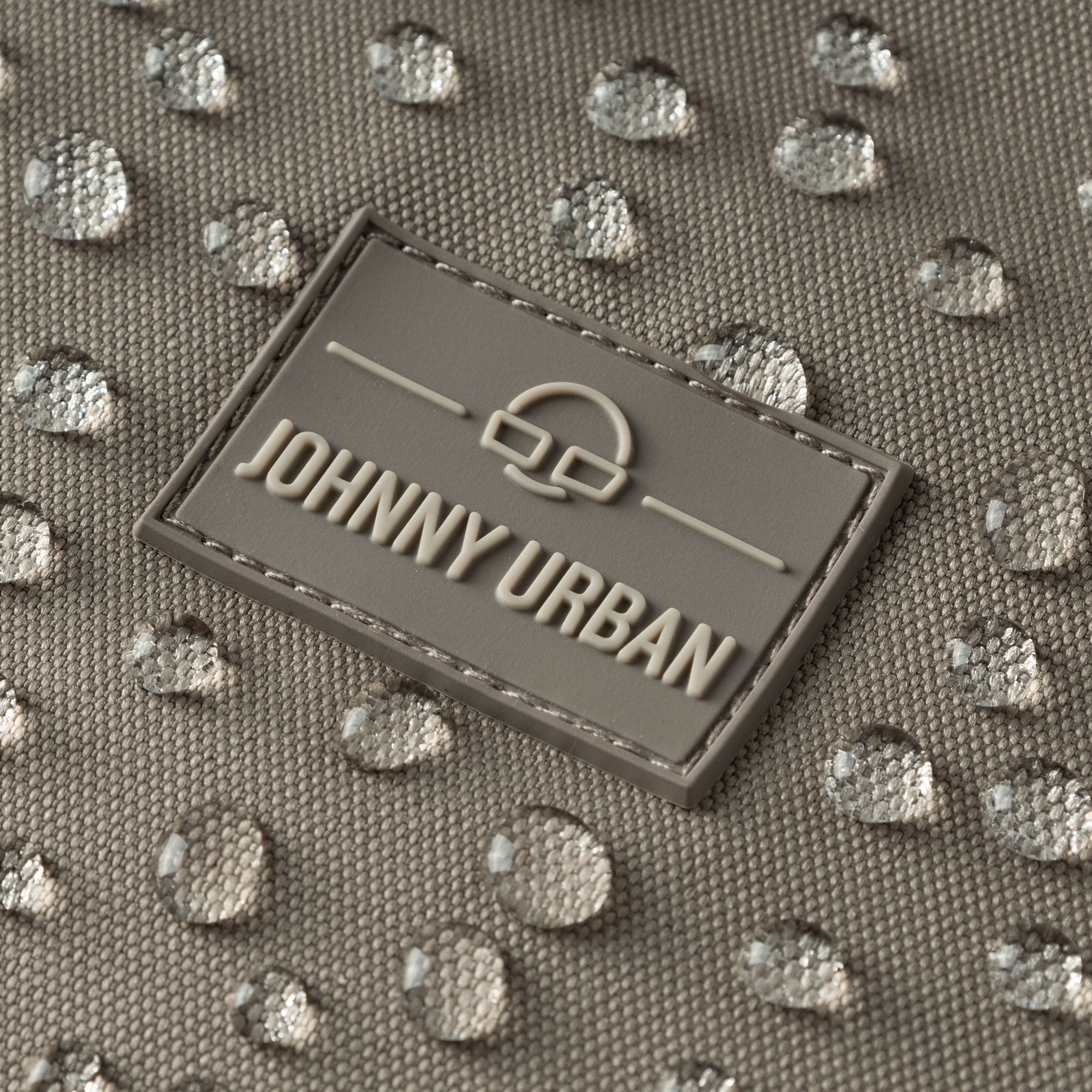 Detailaufnahme des wasserabweisenden hellgrauen Johnny Urban Rolltop Rucksacks mit Logo-Patch und Wassertröpfchen