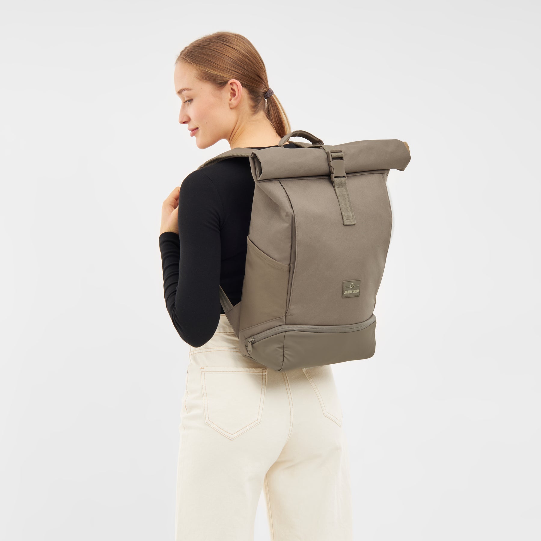 Frau trägt braunen Johnny Urban Rolltop Rucksack 'Allen Medium' mit schwarzem Oberteil und heller Hose