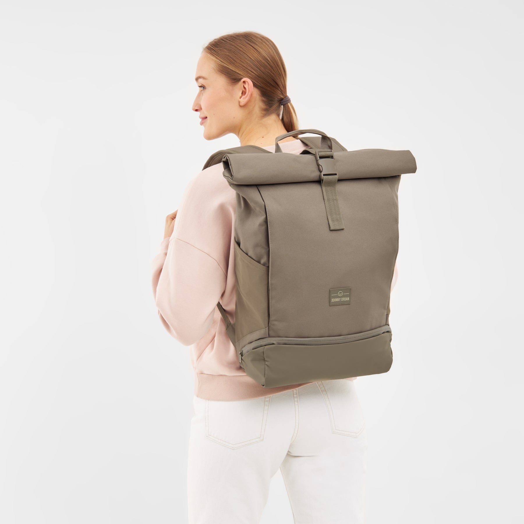 Frau mit zurückgebundenem Haar trägt den Rolltop Rucksack 'Allen Large' in desert grey braun, seitlich aufgenommen