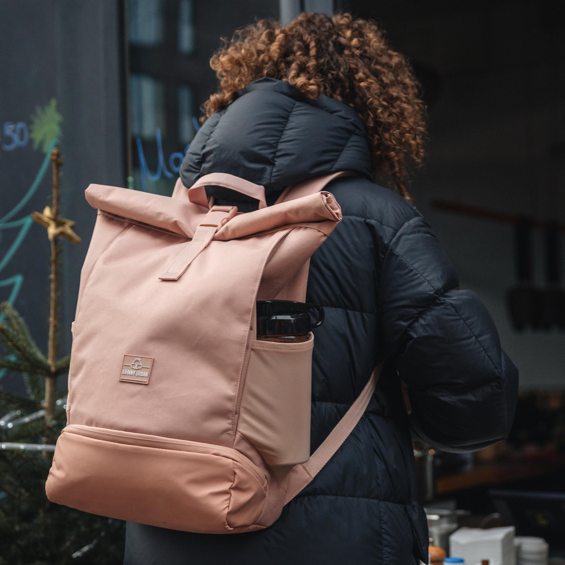 Frau von hinten mit schwarzer Steppjacke trägt rosa Rolltop Rucksack 'Allen Large' von Johnny Urban