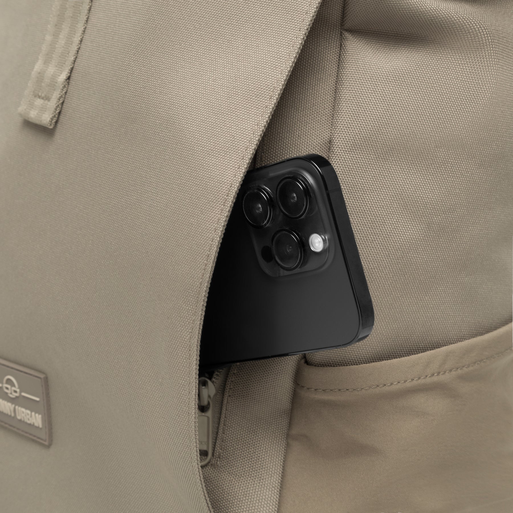 Rolltop Rucksack Allen Medium in desertgrau mit offenem Geheimfach und einem schwarzen Smartphone darin