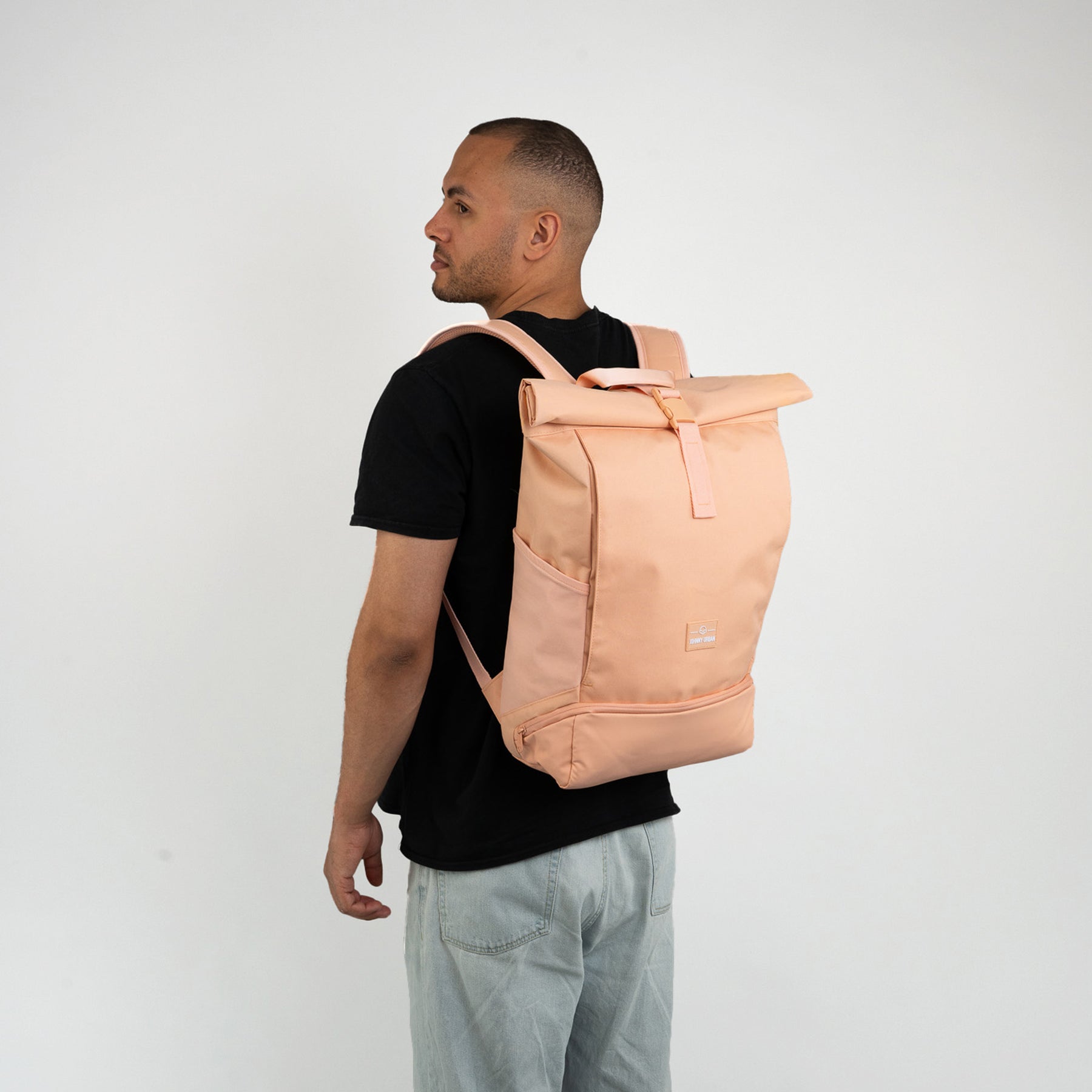Mann trägt pfirsichfarbenen Rolltop-Rucksack 'Allen Large' mit seitlichen Taschen