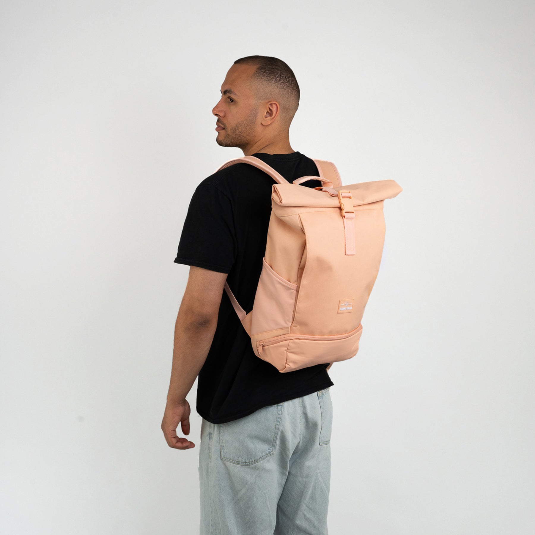 Mann trägt einen pfirsichfarbenen Rolltop Rucksack 'Allen Medium' mit schwarzen T-Shirt und hellen Jeans