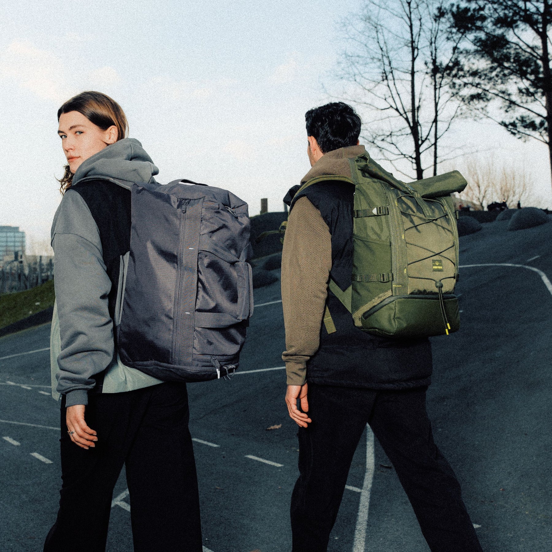 Zwei Personen gehen eine Straße entlang, tragen große Rolltop-Rucksäcke in Grau und Olivgrün