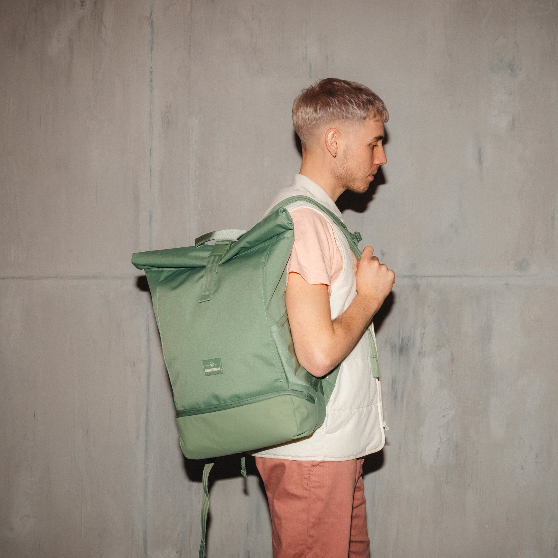 Mann im Profil mit hellgrünem Rolltop Rucksack 'Allen Large' vor Betonwand