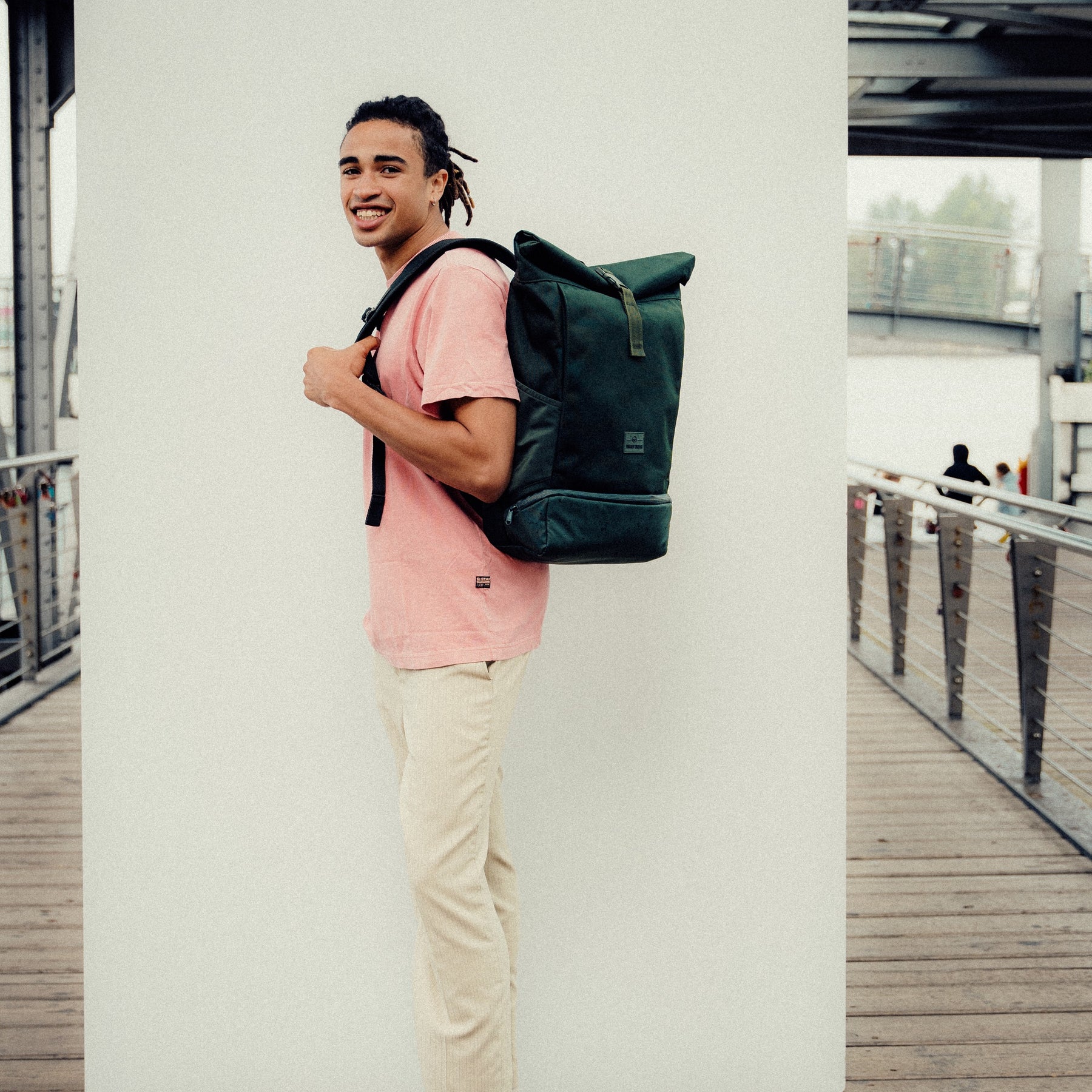 Junger Mann trägt einen schwarzen Johnny Urban Rolltop Rucksack 'Allen Medium' und lächelt