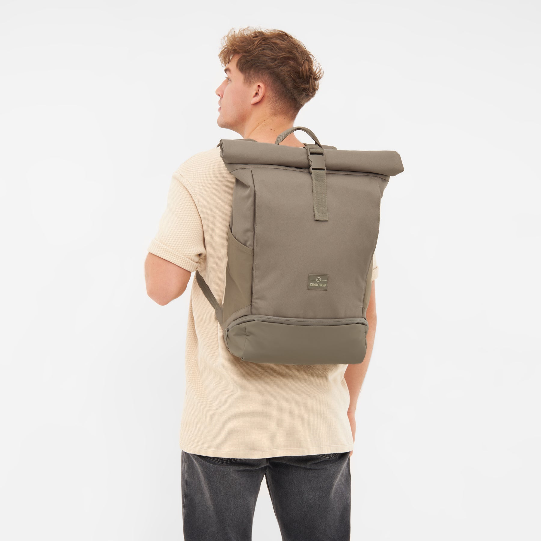 Mann trägt Rolltop Rucksack Allen Large in desert grey Braun auf dem Rücken, Blick nach links