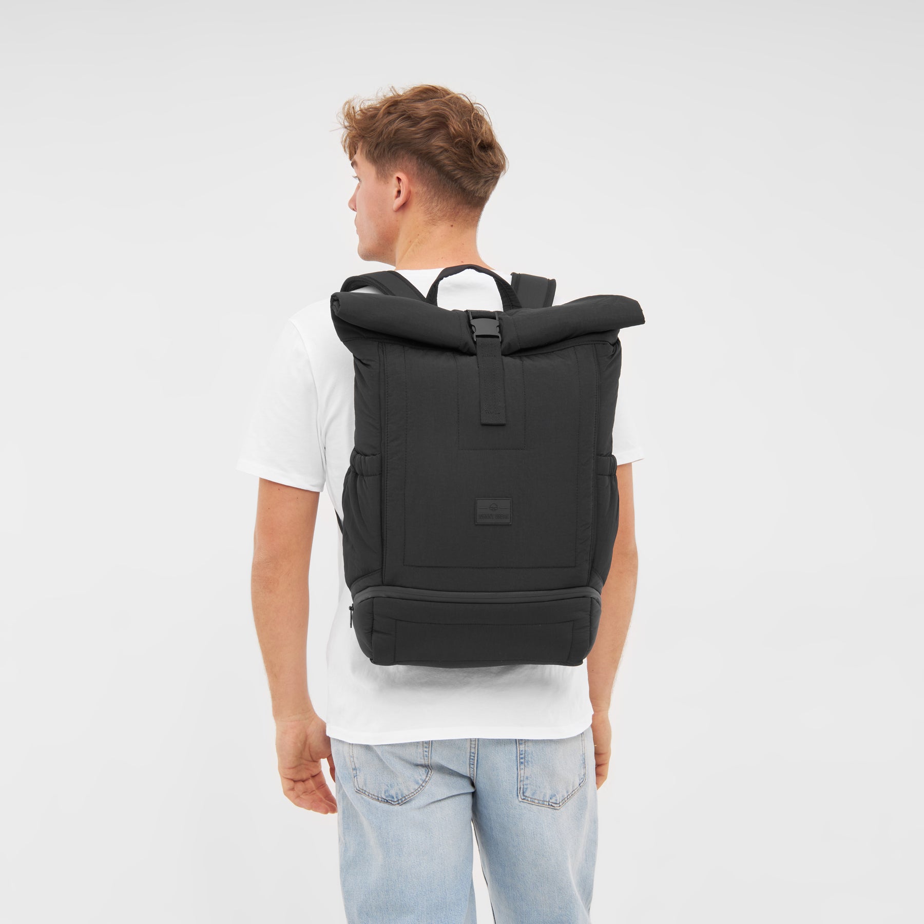 Mann mit weißem T-Shirt und Hellblauen Jeans trägt schwarzen Rolltop Rucksack 'Kyle' von Johnny Urban