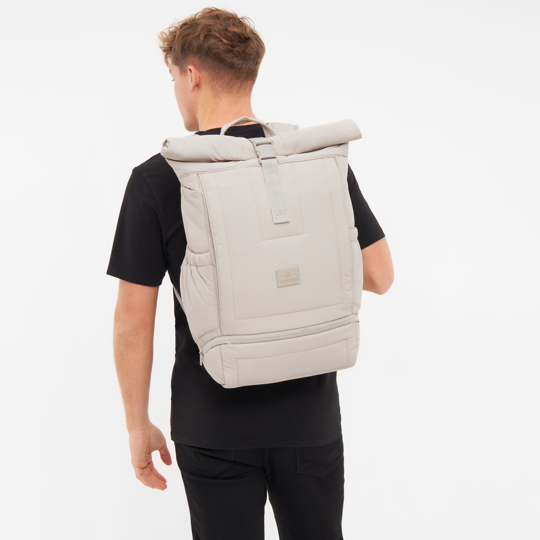 Beiger gepolsterter Rolltop-Rucksack 'Kyle' von Johnny Urban auf dem Rücken eines Mannes in schwarzem T-Shirt.