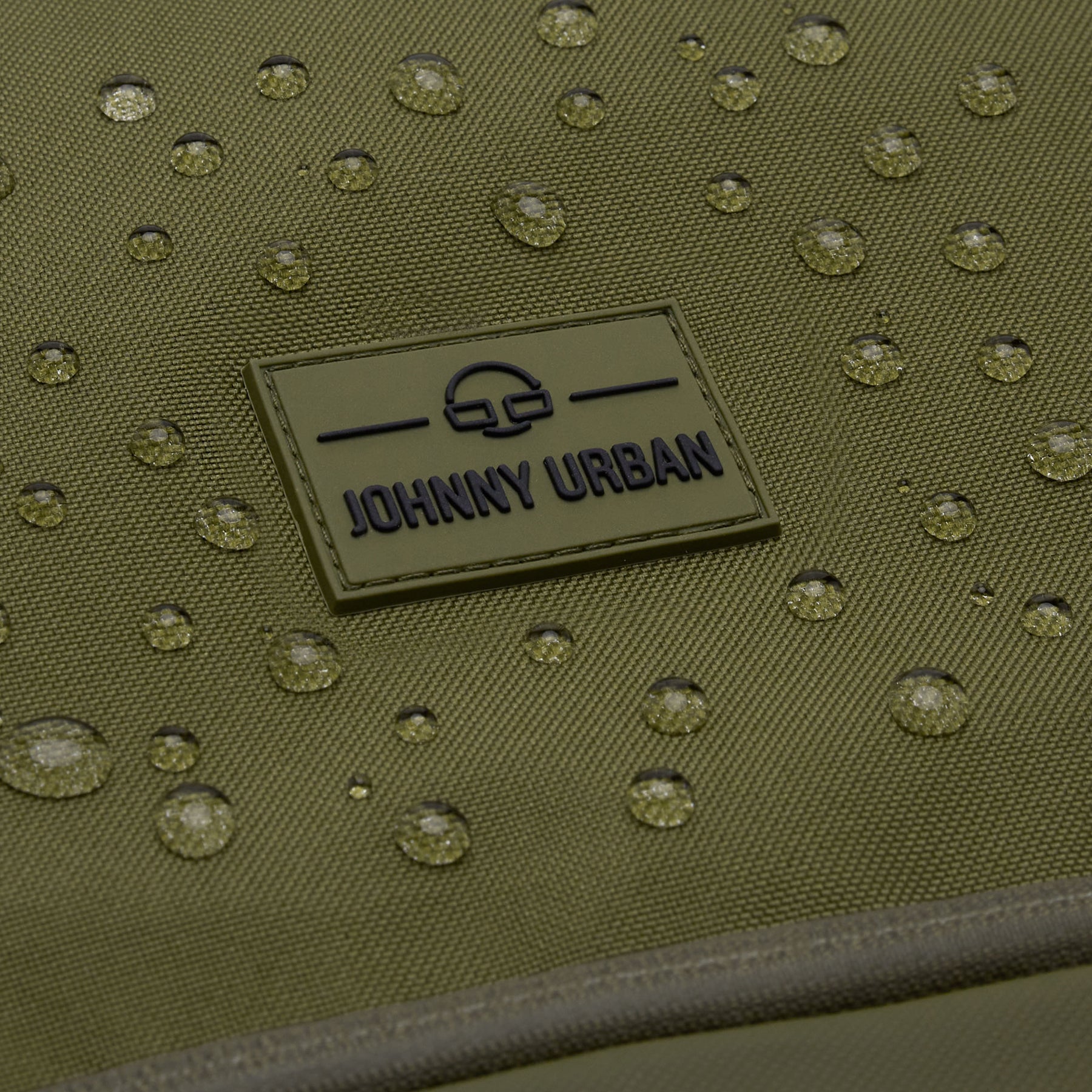 Nahaufnahme des wasserabweisenden olivgrünen Rolltop Rucksacks ‚Allen Medium‘ mit Johnny Urban Logo und Wassertropfen