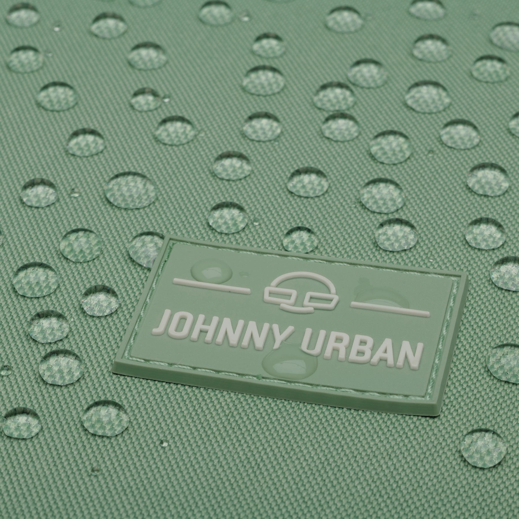 Grünes, wasserdichtes Material mit Johnny Urban Logo und Wasserperlen darauf