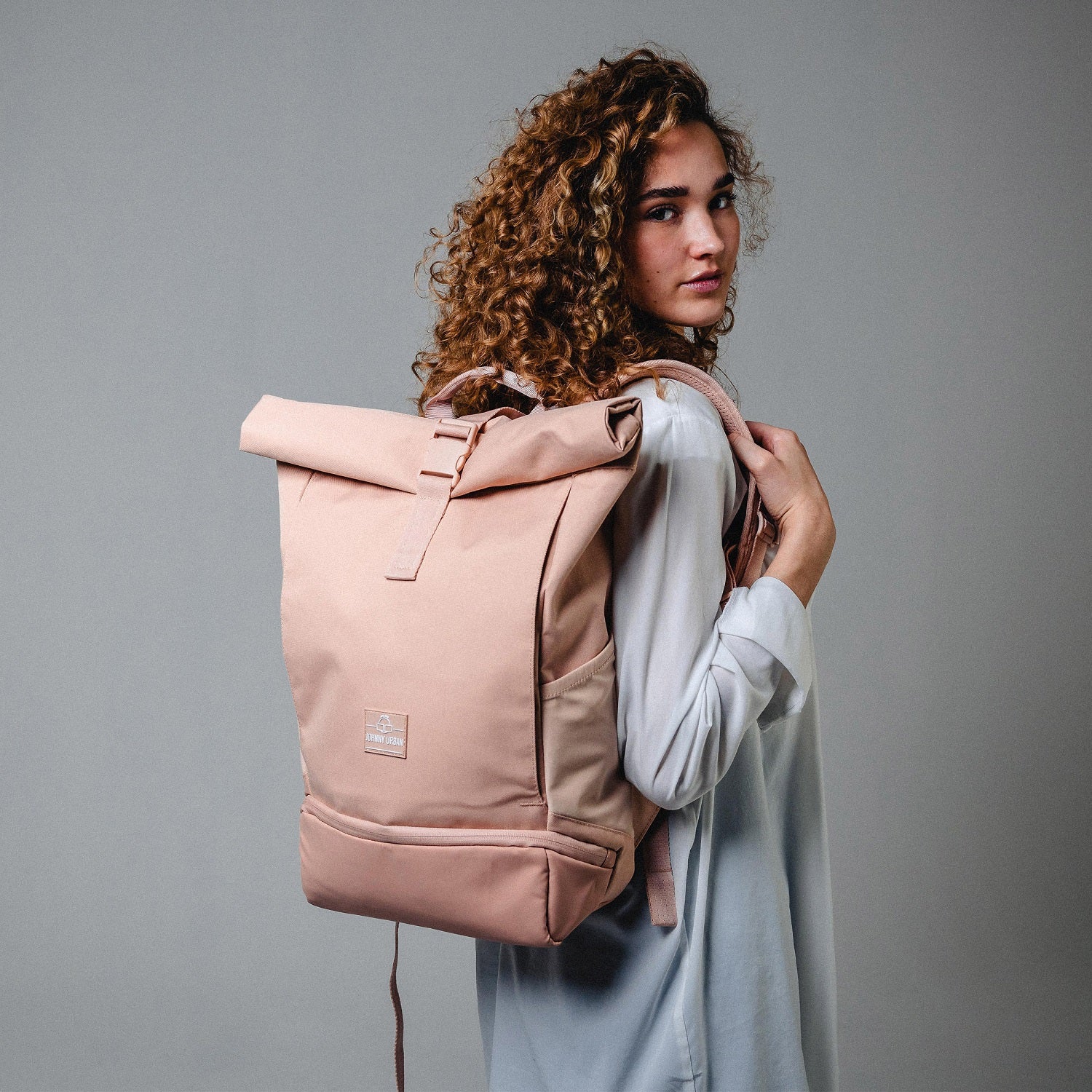 Frau mit lockigem Haar trägt hellrosa Johnny Urban Rolltop Rucksack 'Allen Medium'